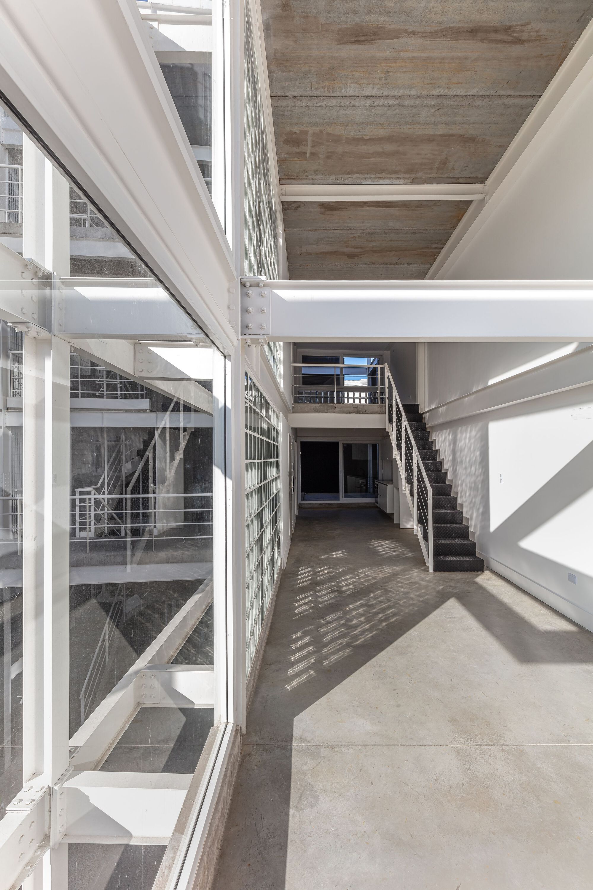 Interior hallway with glass block wall and overlapping steel staircases in afternoon light