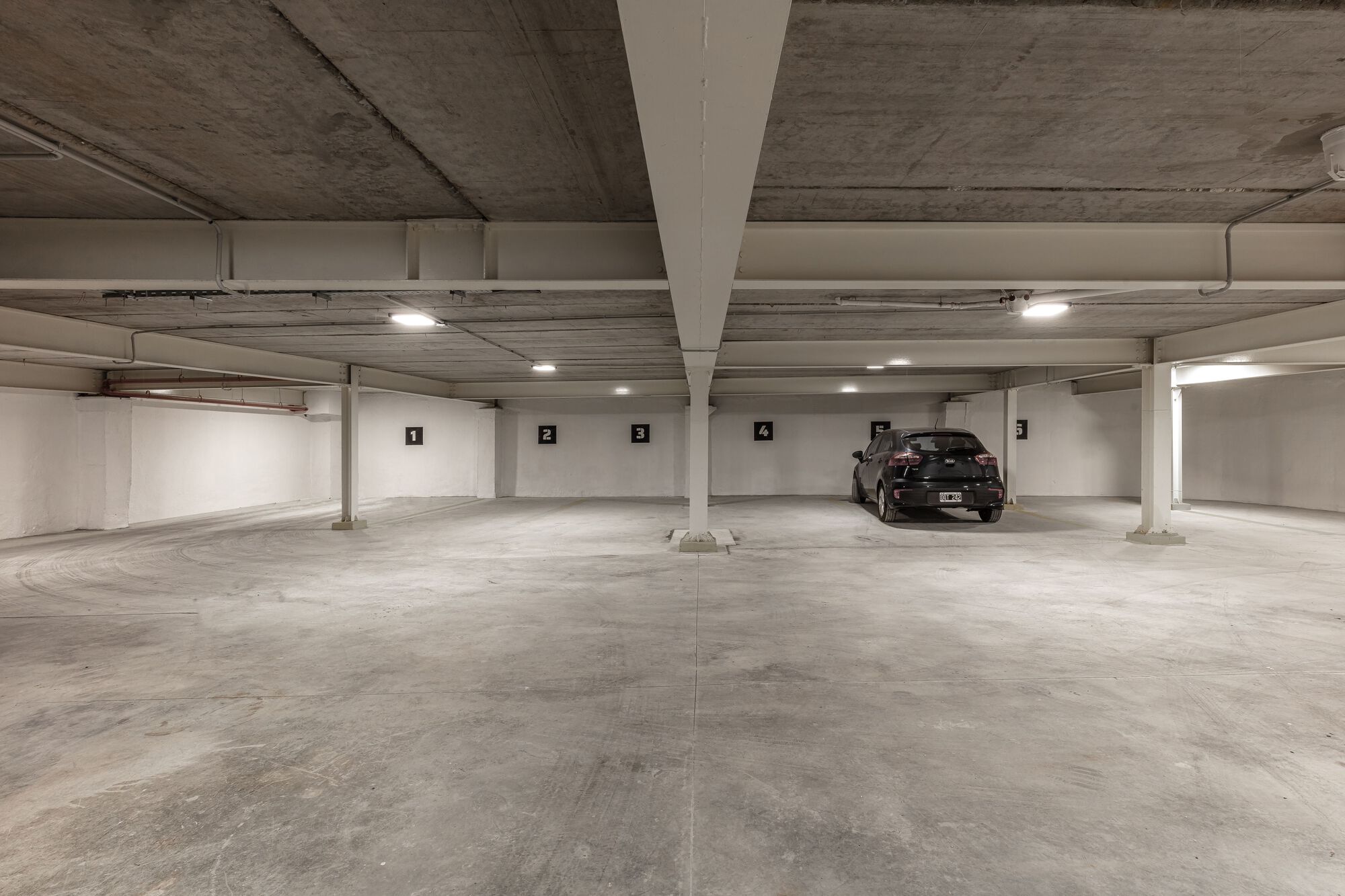 Underground parking level with exposed concrete ceiling, white columns, and numbered parking spaces