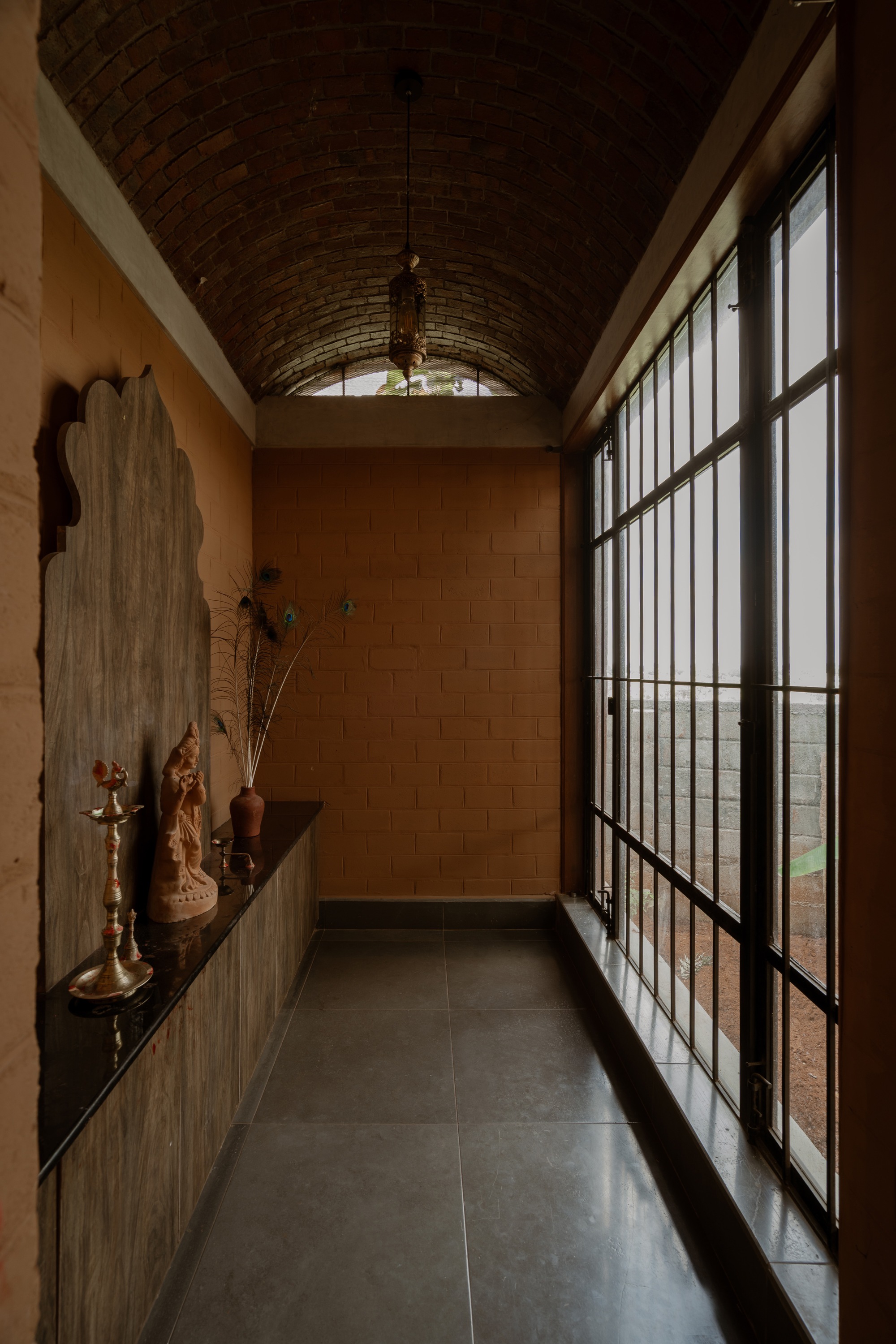 Corridor with gridded steel-frame door opening to landscape beneath a curved brick ceiling vault