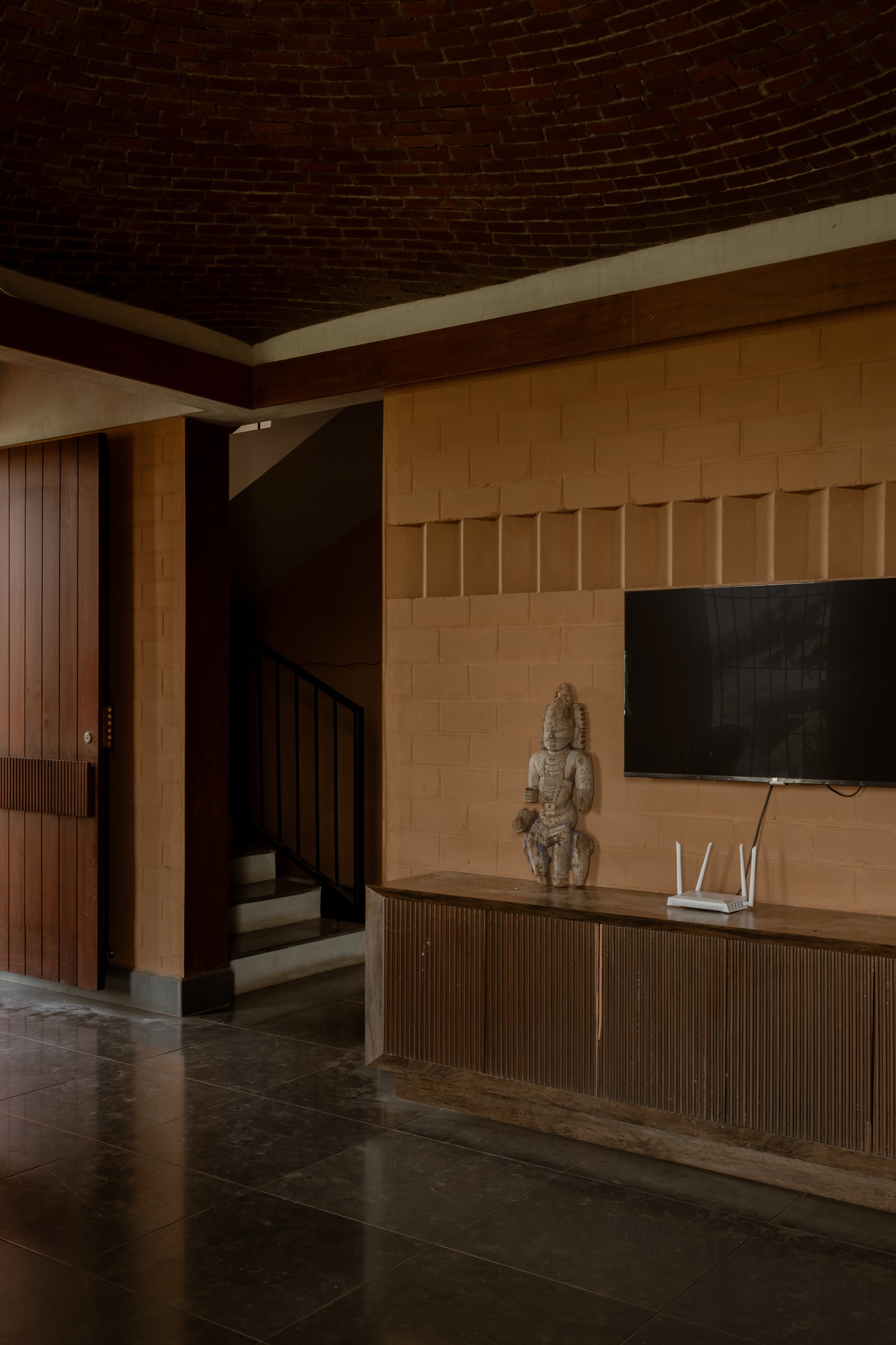 Interior living space with a curved brick vault ceiling above light sandstone walls and dark tile flooring