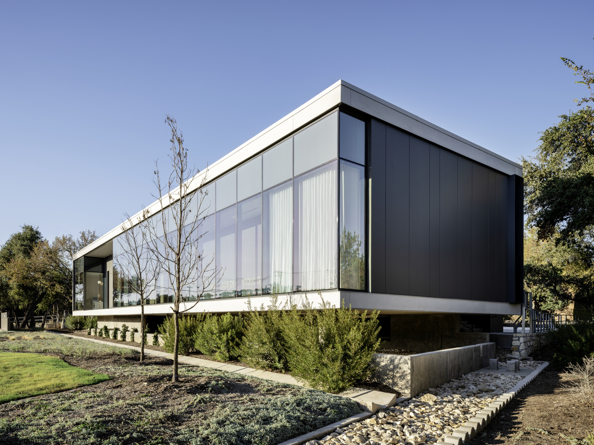 Corner view showing the cantilevered dark metal cladding above a planted slope with young trees