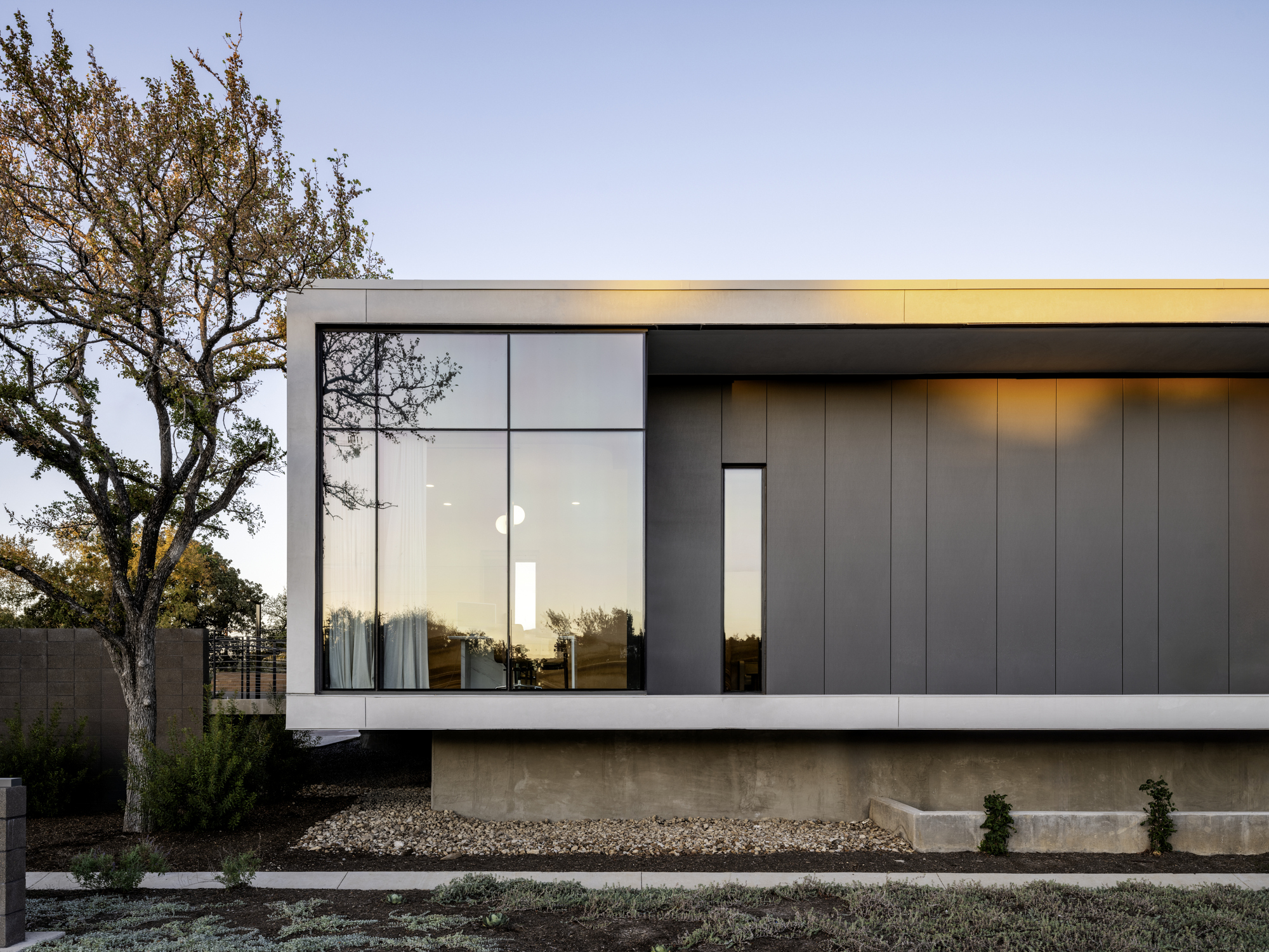 Facade detail of the vertical metal panels meeting the glazed corner beneath a flat roof overhang