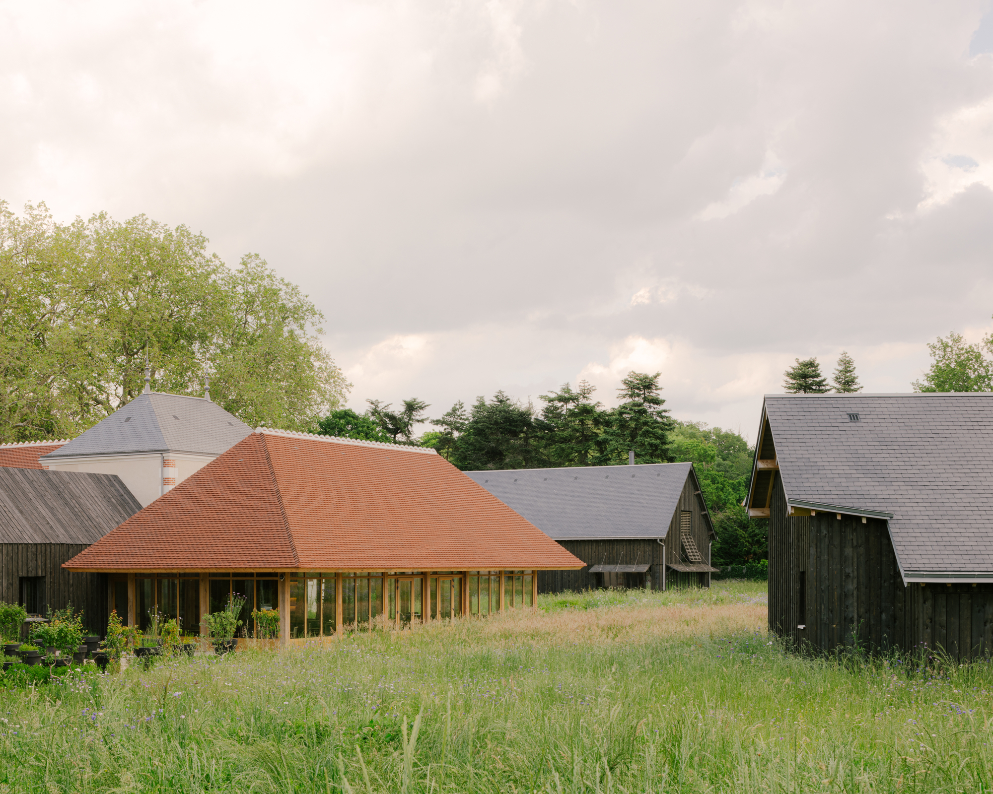 Low-pitched pyramidal roof with terracotta tiles rising above a grassy meadow and surrounding farm buildings