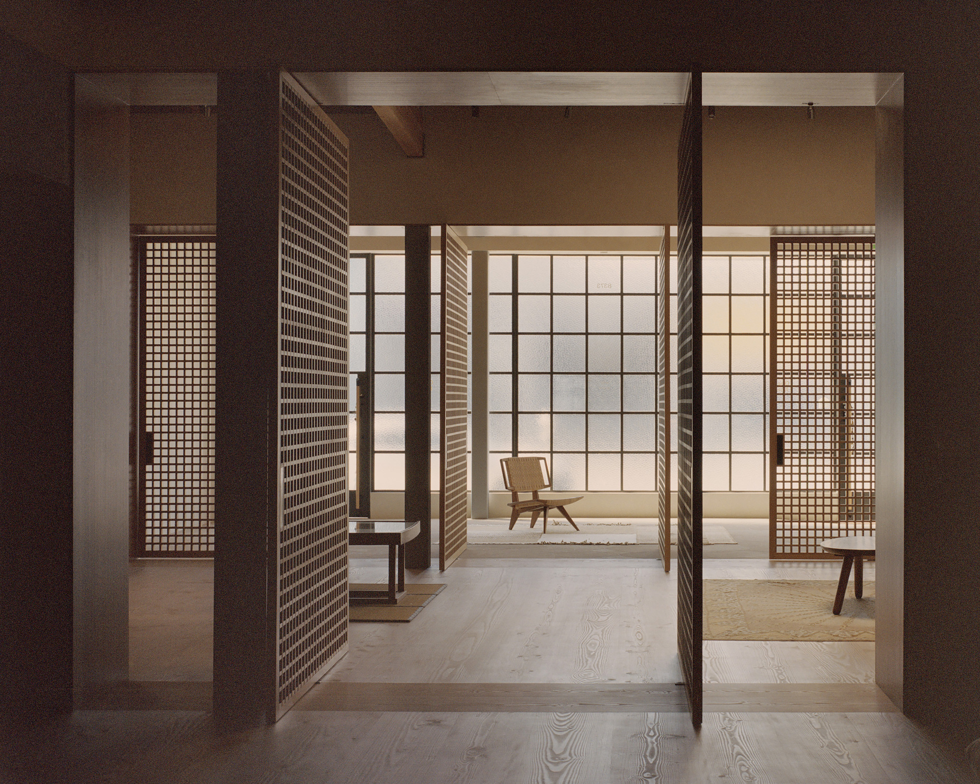 View through pivoting timber lattice screens into a softly lit room with translucent wall panels and exposed ceiling beams