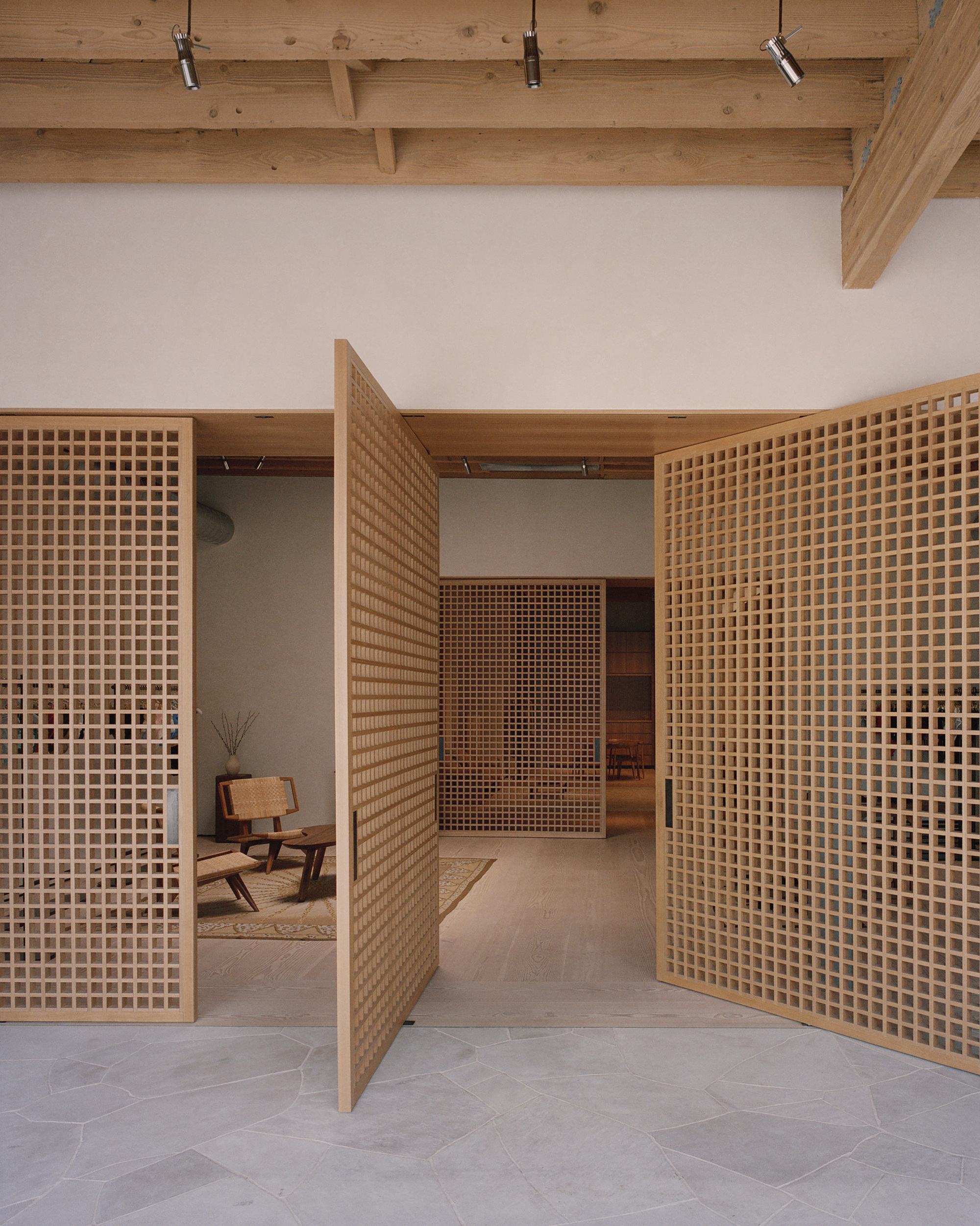 Timber lattice partition walls with square grid openings framing a seated area beneath a beam ceiling with track lighting