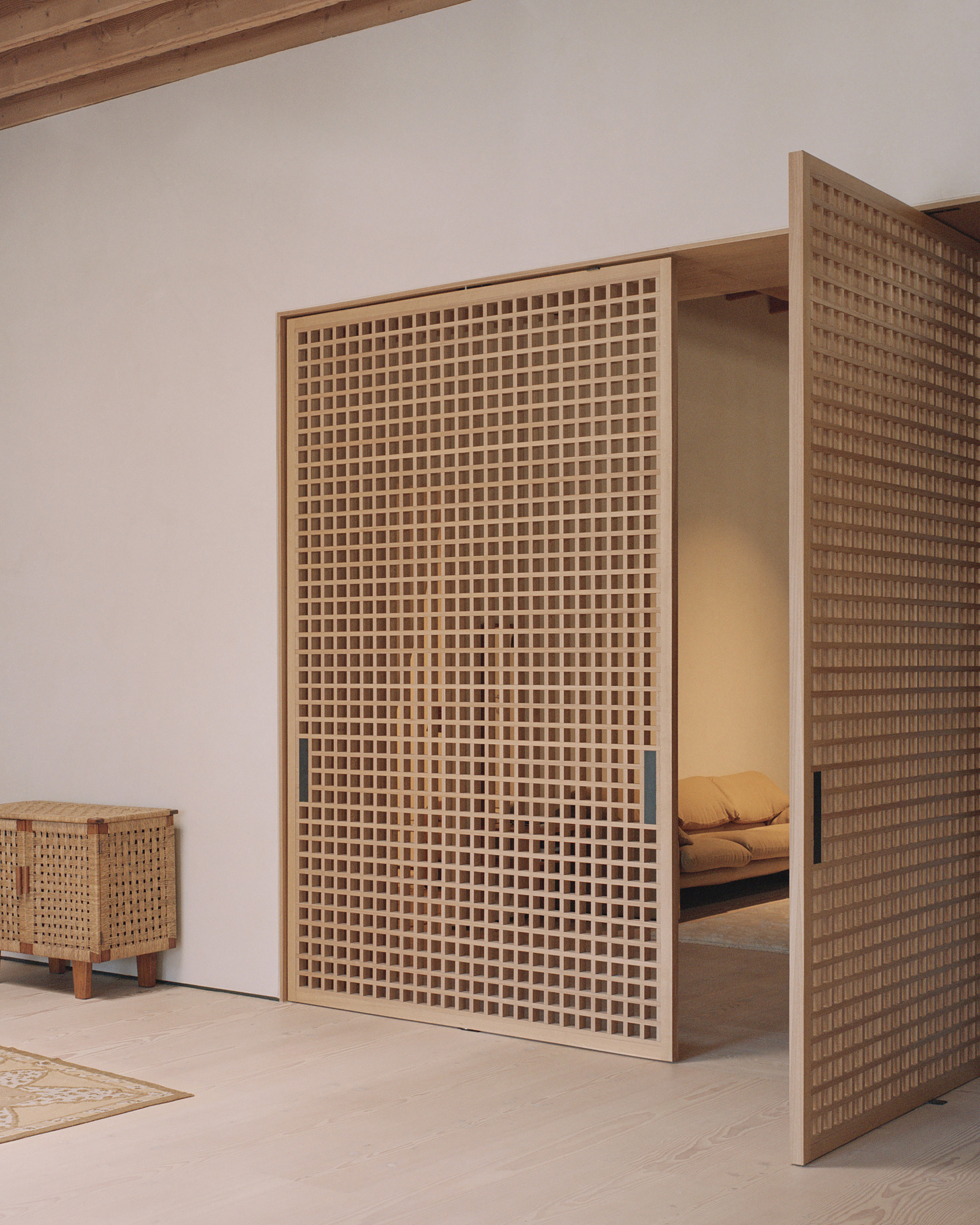Close-up of a tall timber lattice screen with visible bedroom space beyond a narrow opening in the white wall