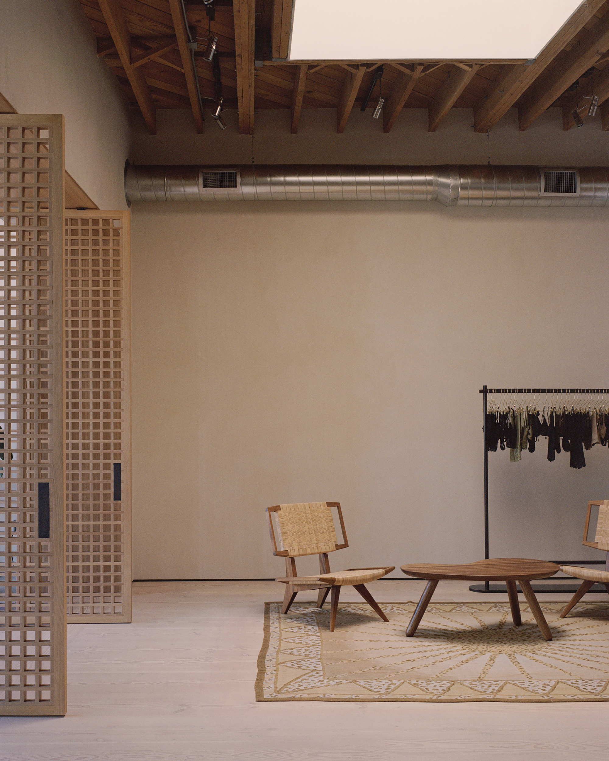 Retail interior with latticed timber partitions, exposed ductwork, timber furniture, and clothing rack on patterned rug