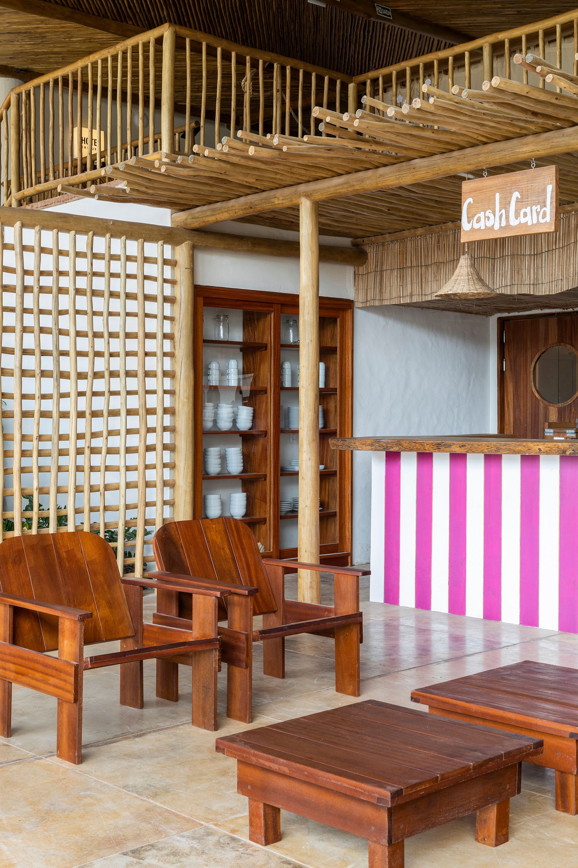 Interior seating area with timber furniture, lattice screen wall and pink-striped counter under exposed bamboo rafters