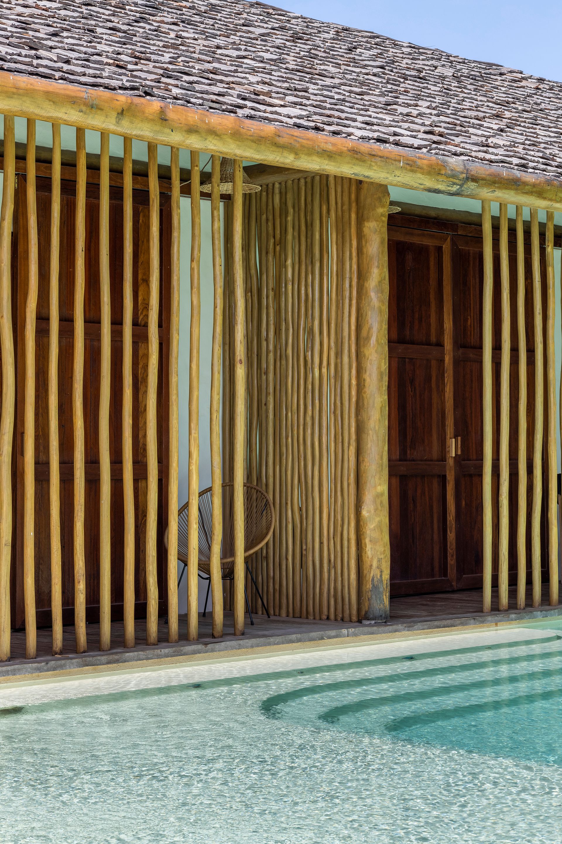 Close view of the timber louvered facade with sliding panel and carved wooden door beside the pool
