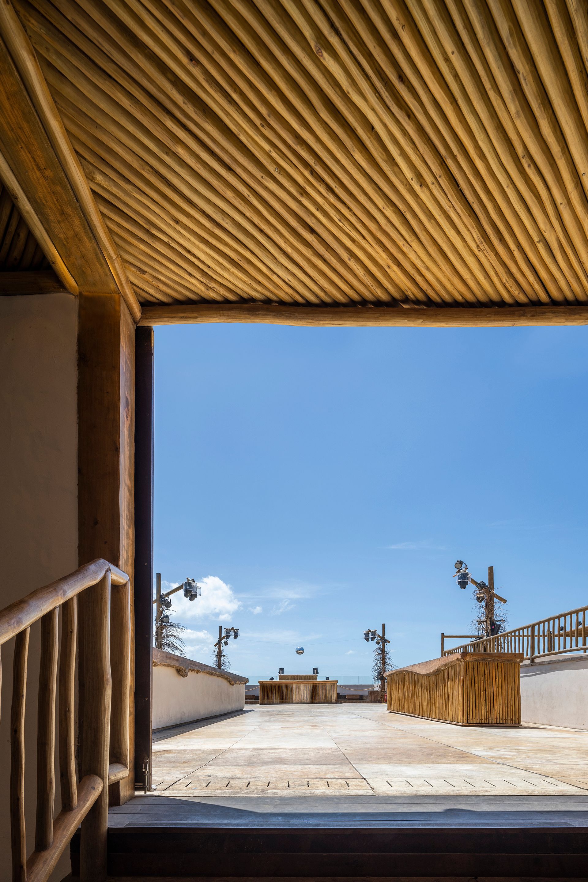 Diagonal bamboo ceiling framing a doorway that opens onto a terrace under clear blue sky