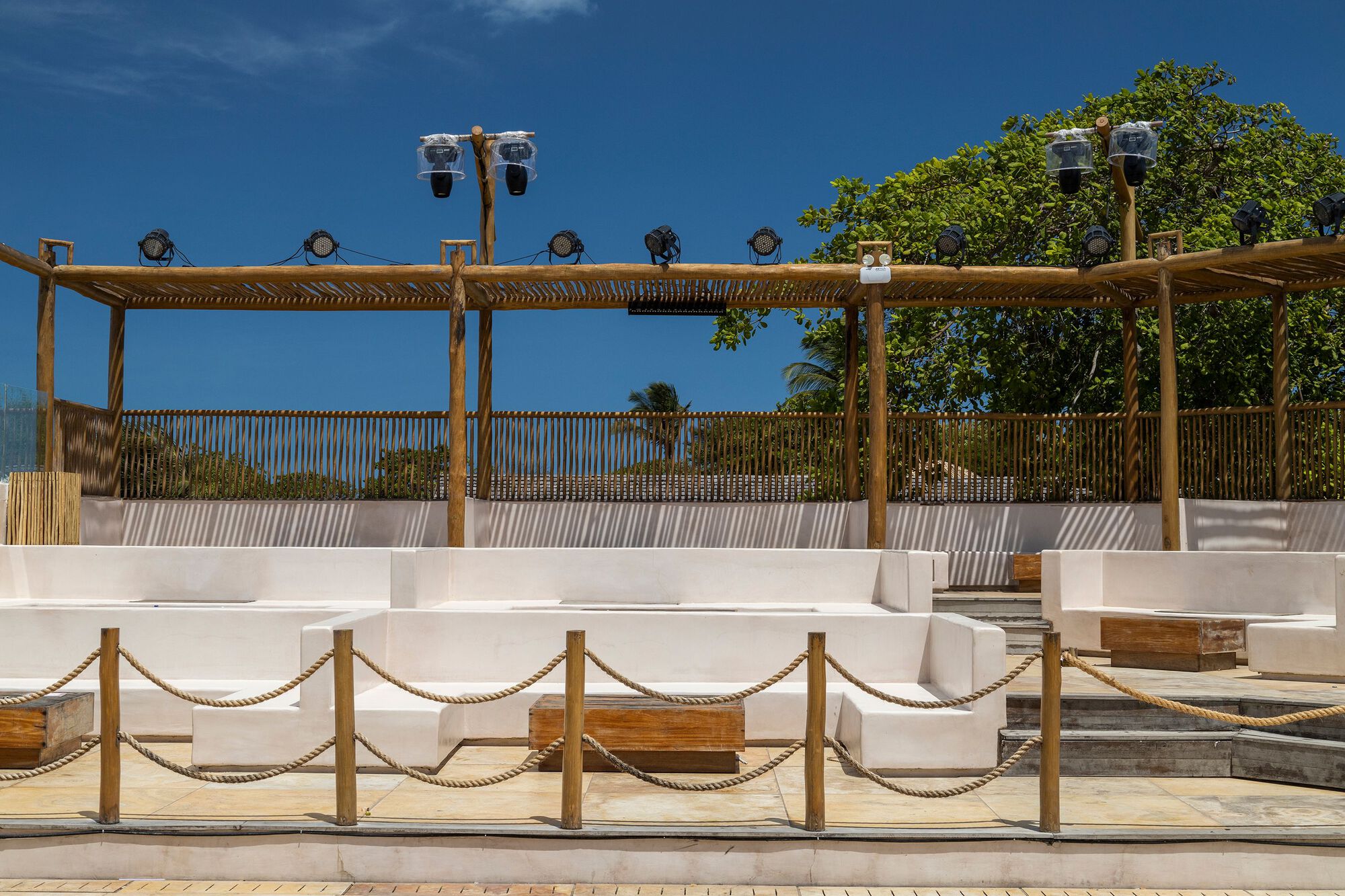 Tiered white concrete seating with rope railings beneath timber pergola and theatrical lighting fixtures