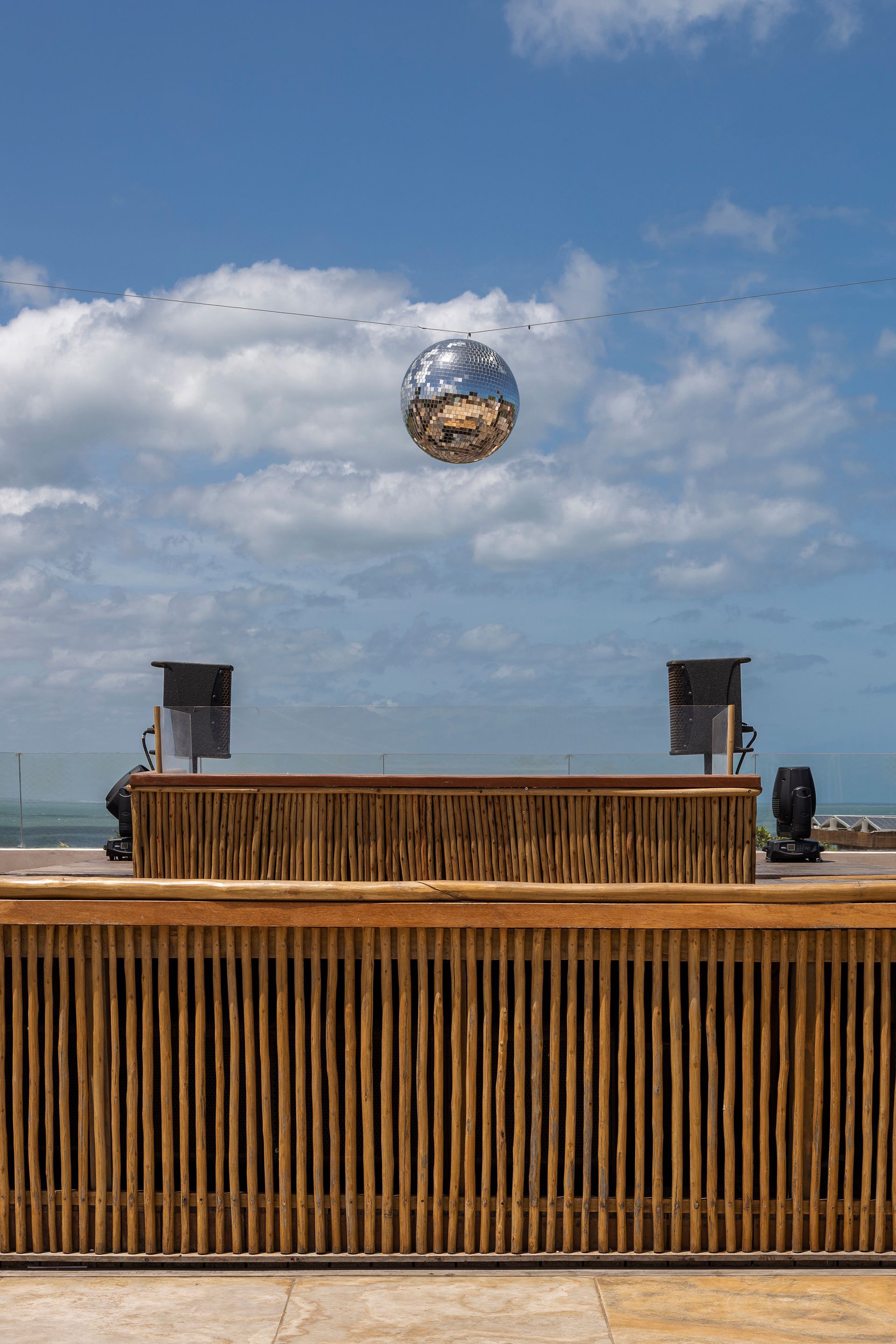 Timber slatted bar counter with speakers and mirrored disco ball suspended above the ocean terrace