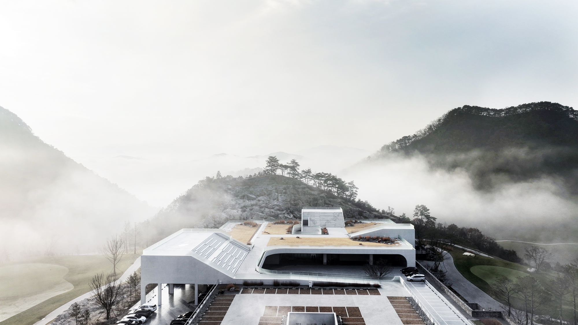 The layered building with curved rooflines and vegetated terraces surrounded by morning mist in the valley
