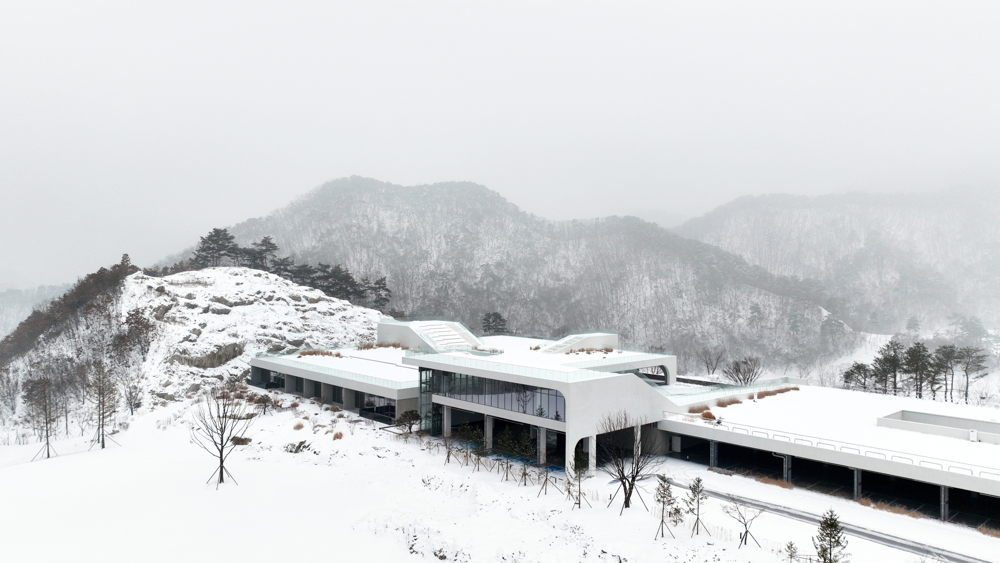 Winter view of the horizontal wings with glazed facades and white roofs stretching across the snowy hillside