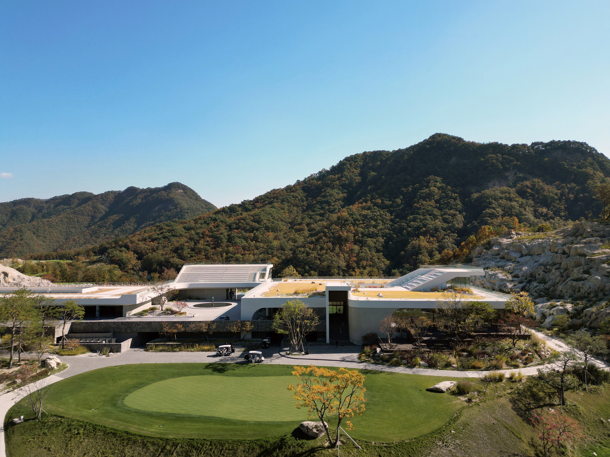 Elevated view of the complex with curved roofs and a circular lawn terrace surrounded by mountains in daylight