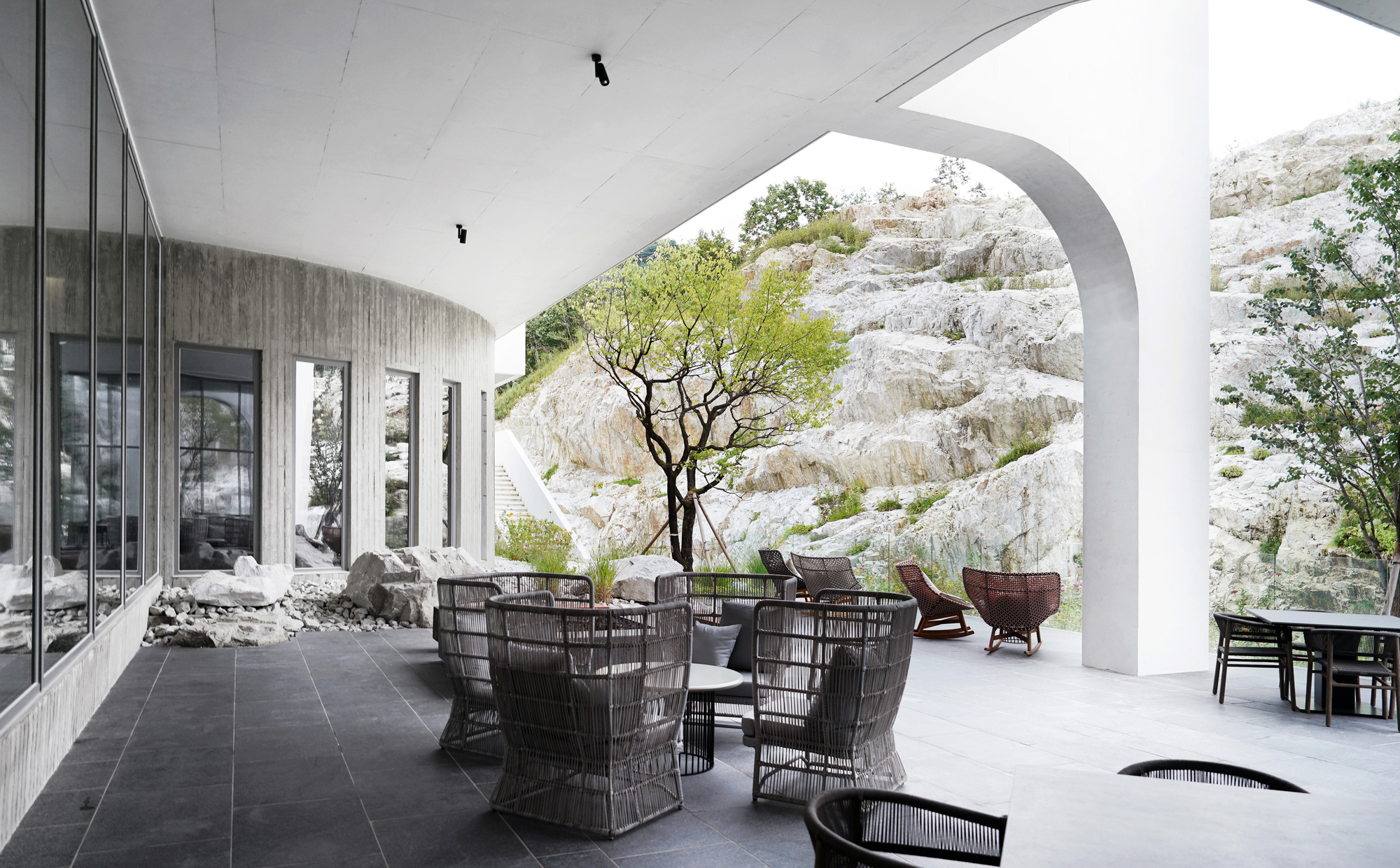 Covered terrace with vaulted white ceiling and dark wicker furniture framed by a large arch opening to rocky hillside