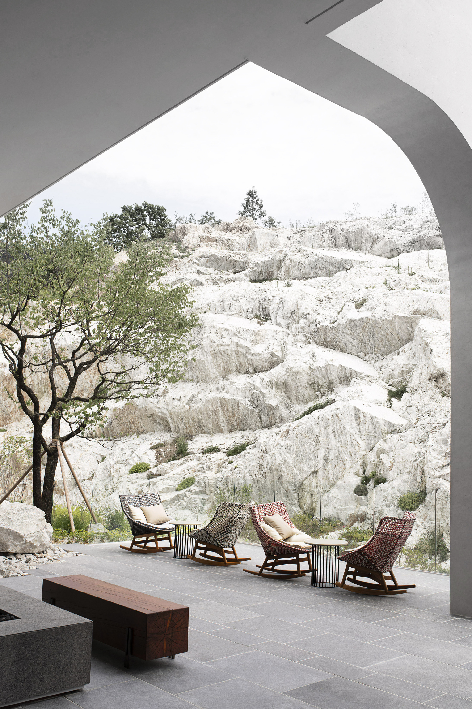 Covered terrace with woven rocking chairs framing a view of white limestone cliffs and a tree