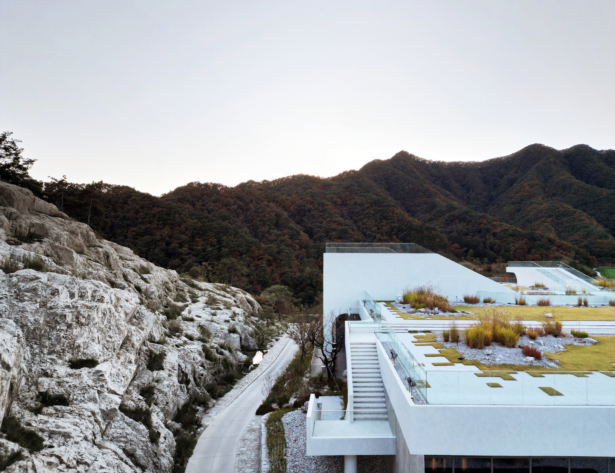 Planted roof terraces stepping down the rocky hillside with forested mountains in the background at dusk