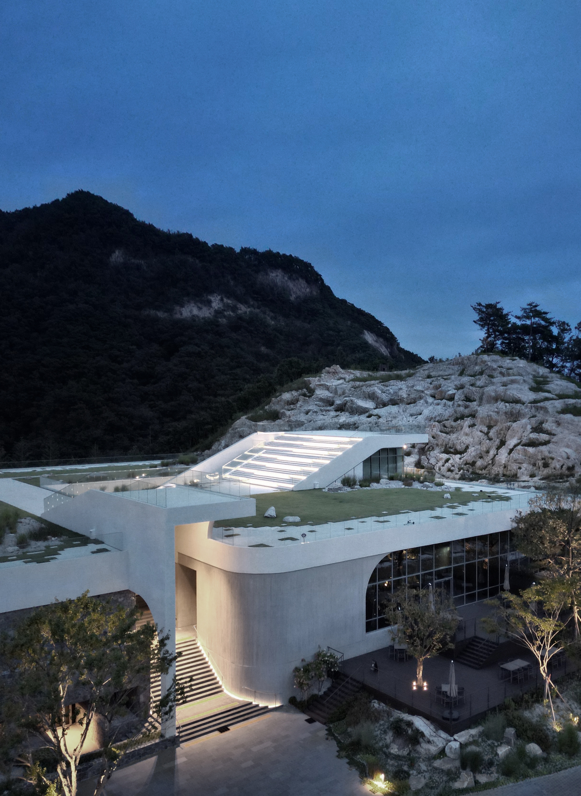 Elevated view of the illuminated entrance volume with curved glass facade and ribbed roof at twilight