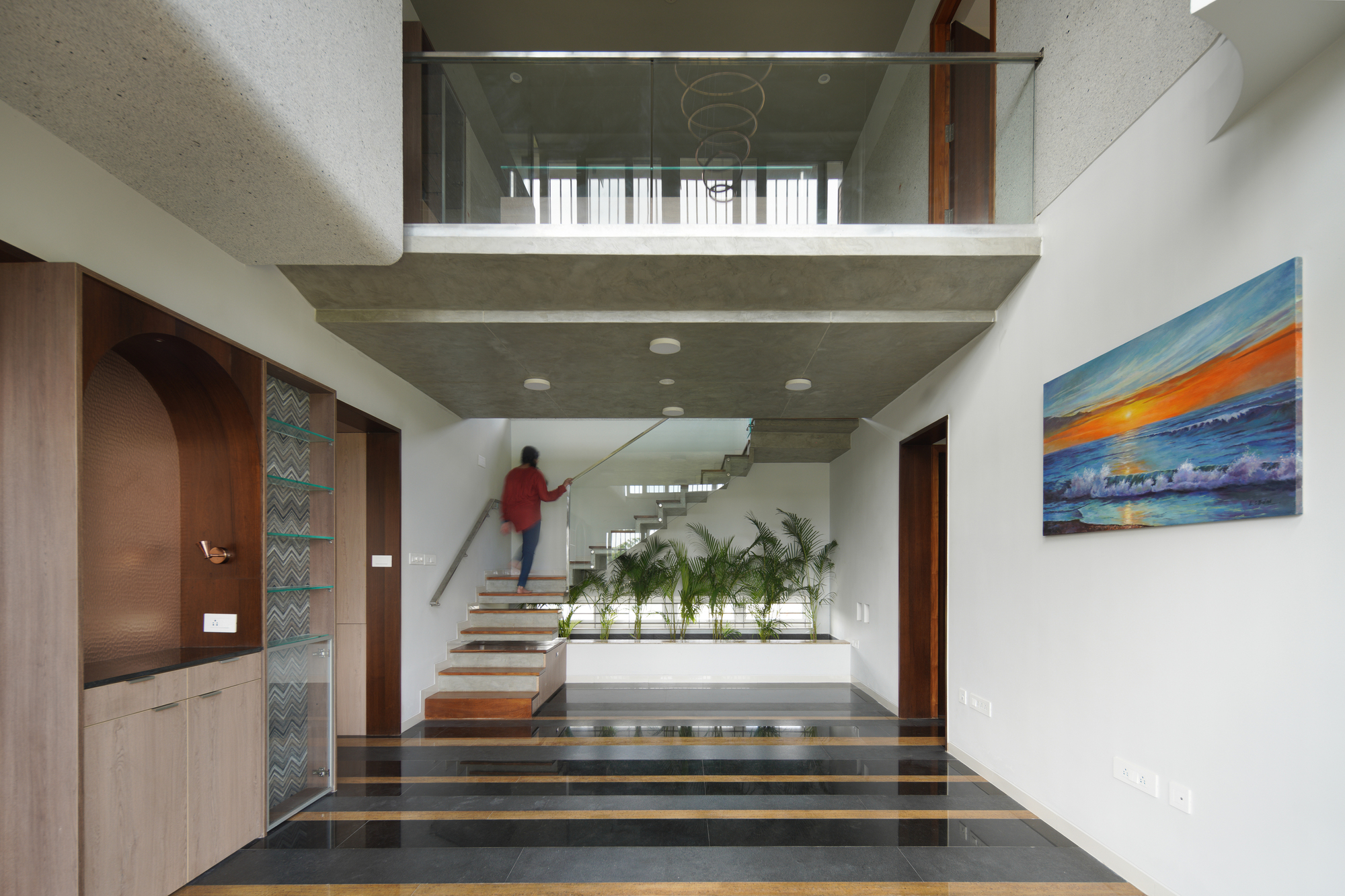 Double-height entry hall with a person ascending the floating staircase beneath a concrete mezzanine