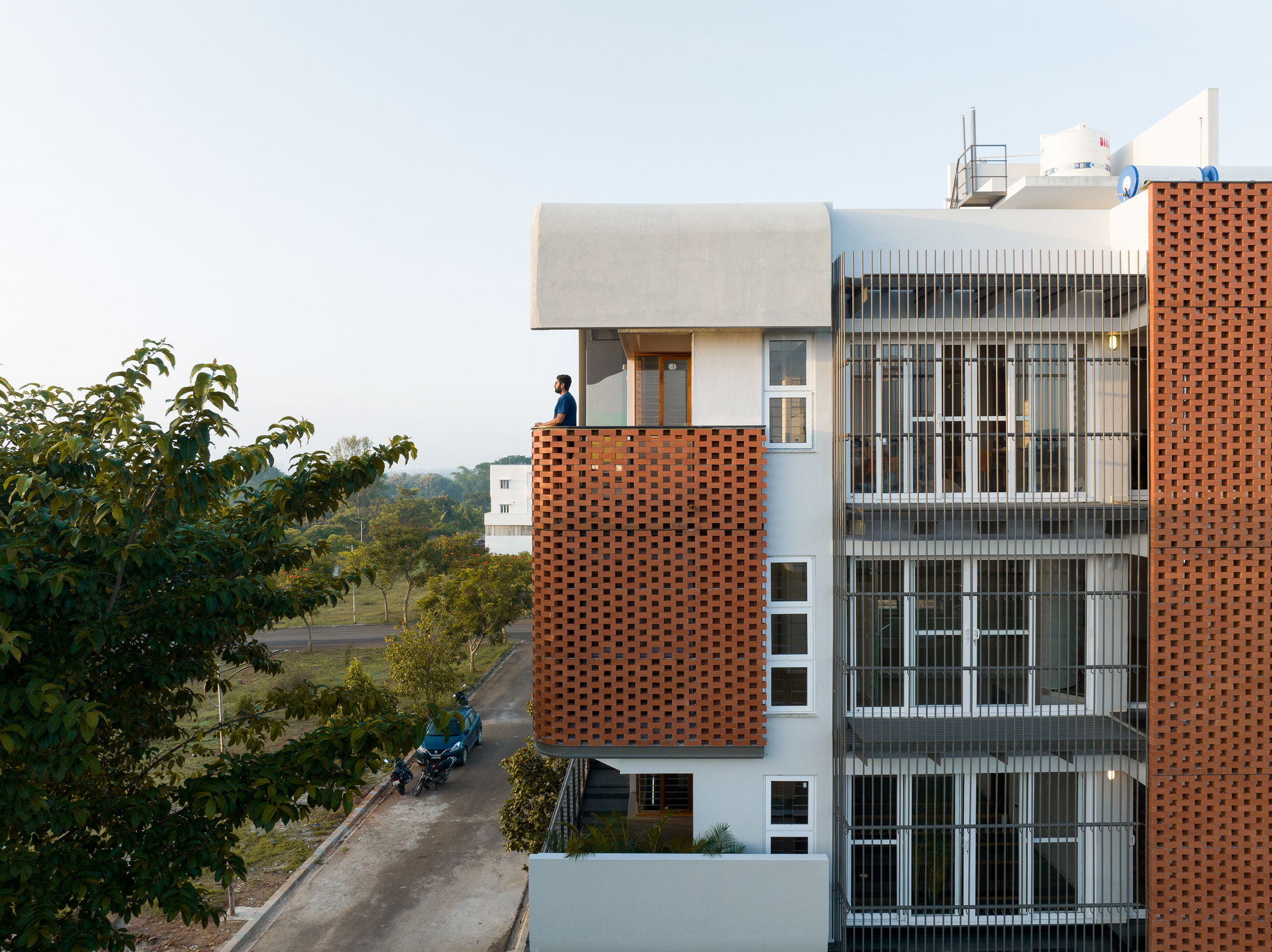 Street view showing the layered facade with a figure on the rooftop terrace at dusk
