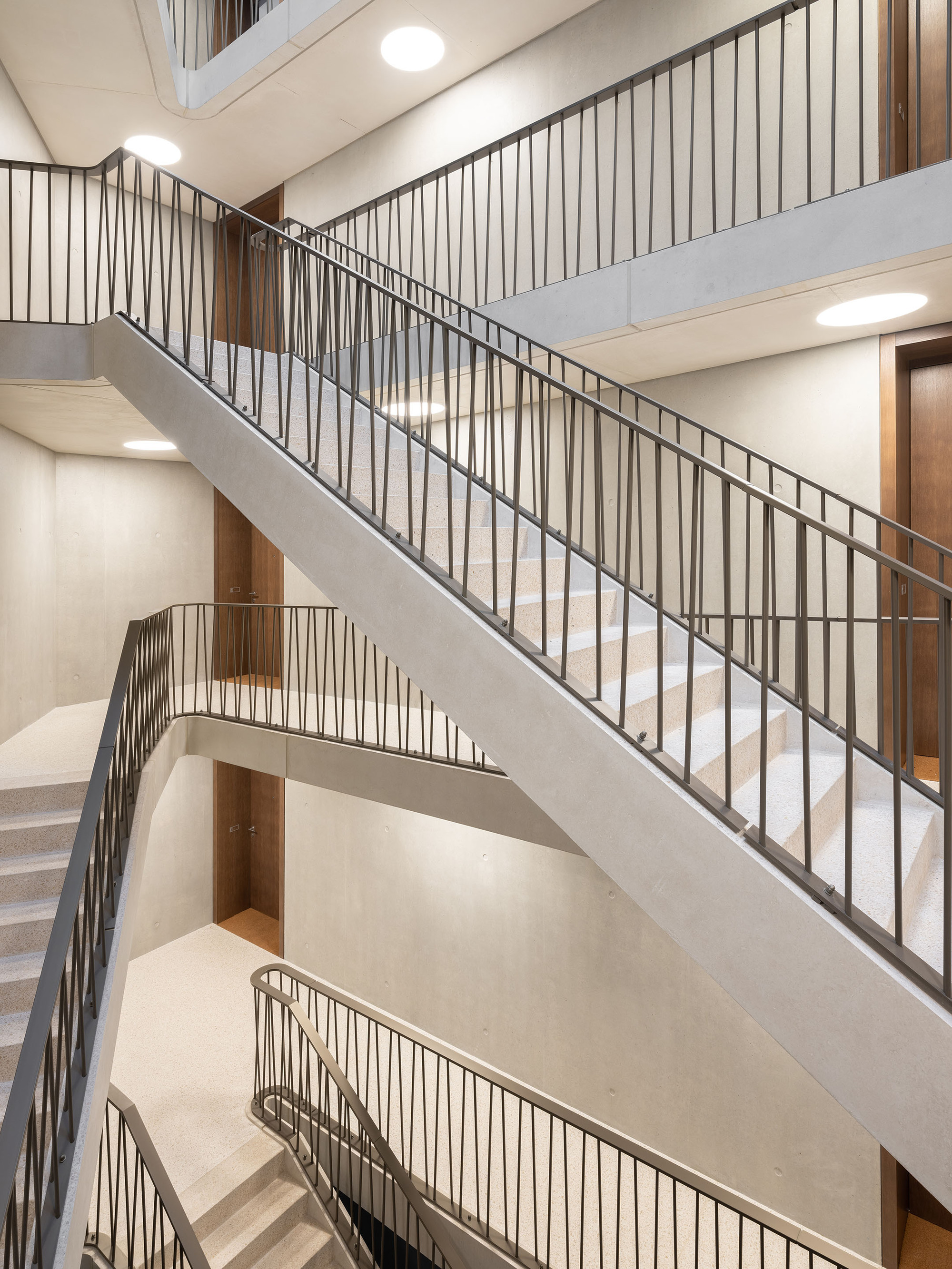 Precast concrete staircase with vertical metal railings and timber-clad landings in artificial light
