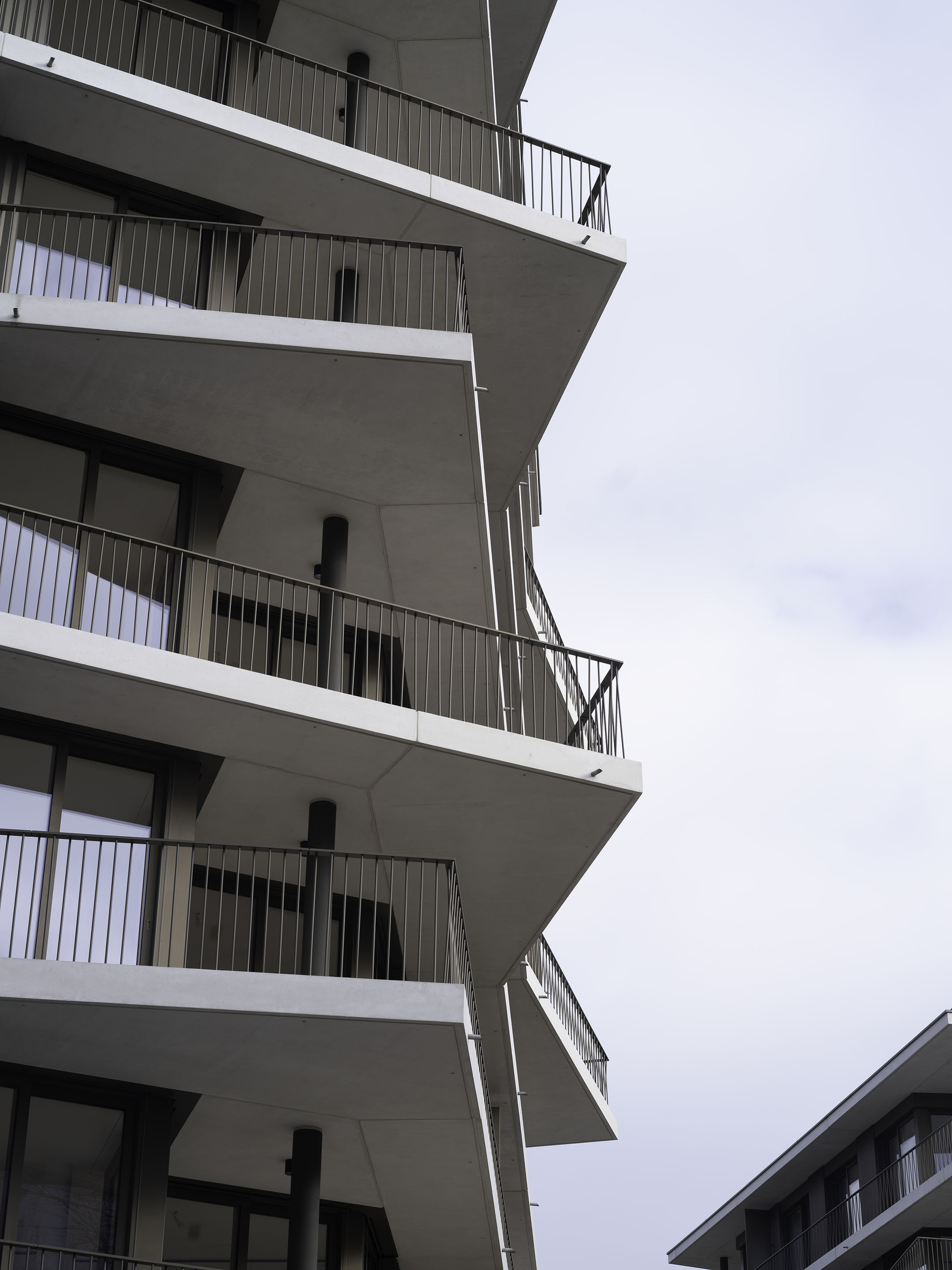 Stacked concrete balconies with protruding slabs and metal railings against an overcast sky