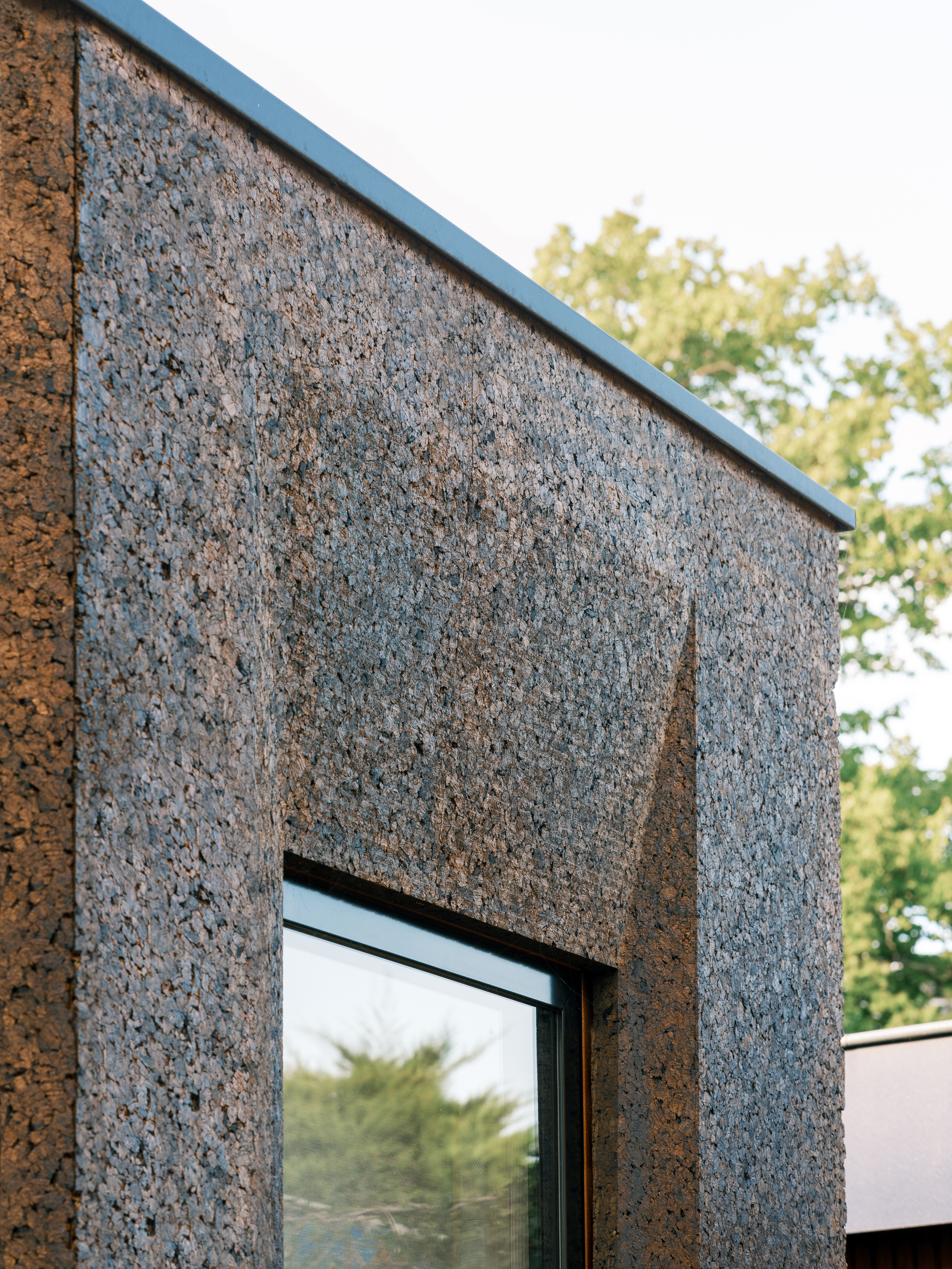 Close-up of the cork cladding panel joint and metal cap edge with trees visible beyond