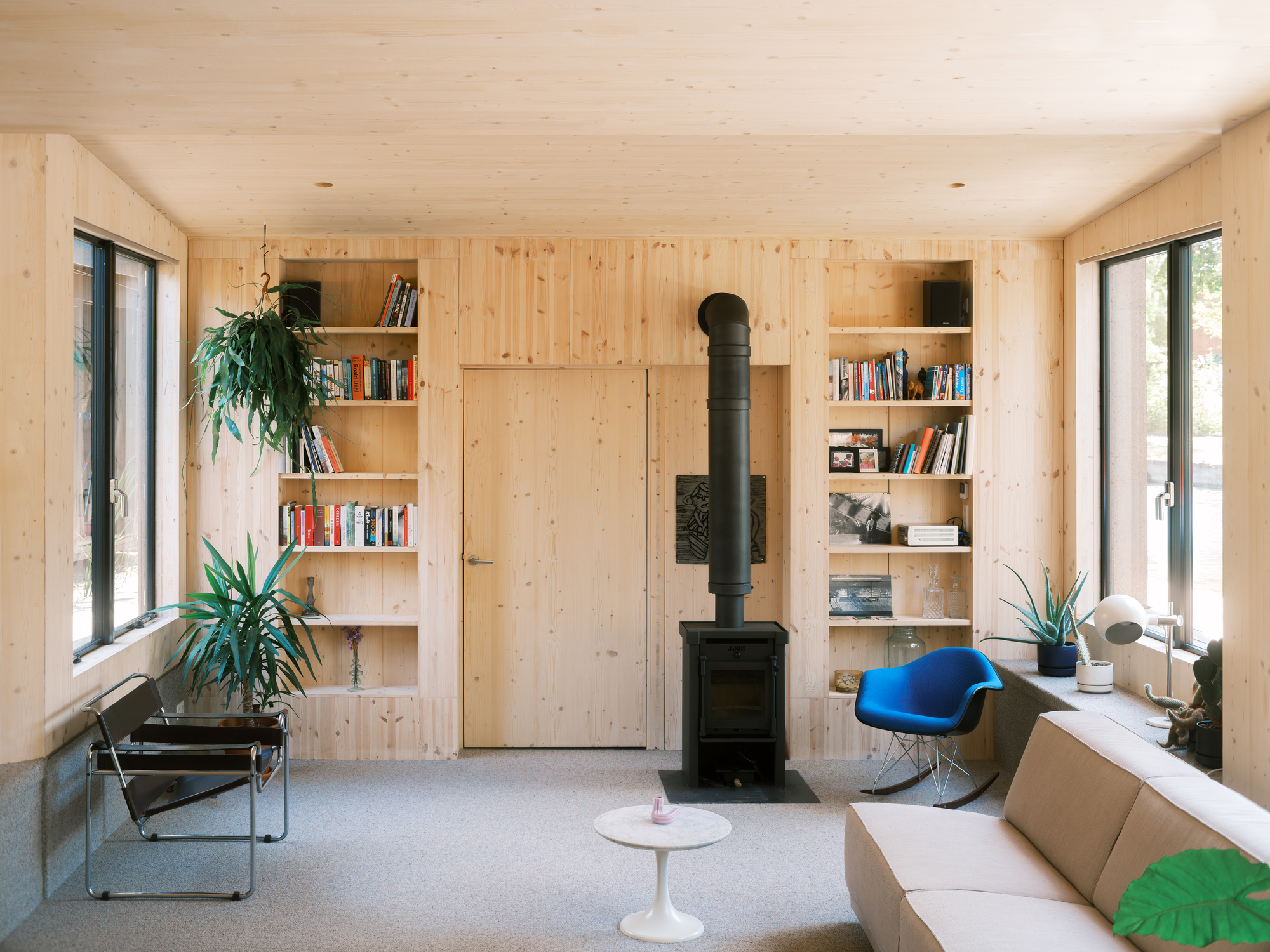 Light timber living room with built-in bookshelves flanking a central wood stove and flush door