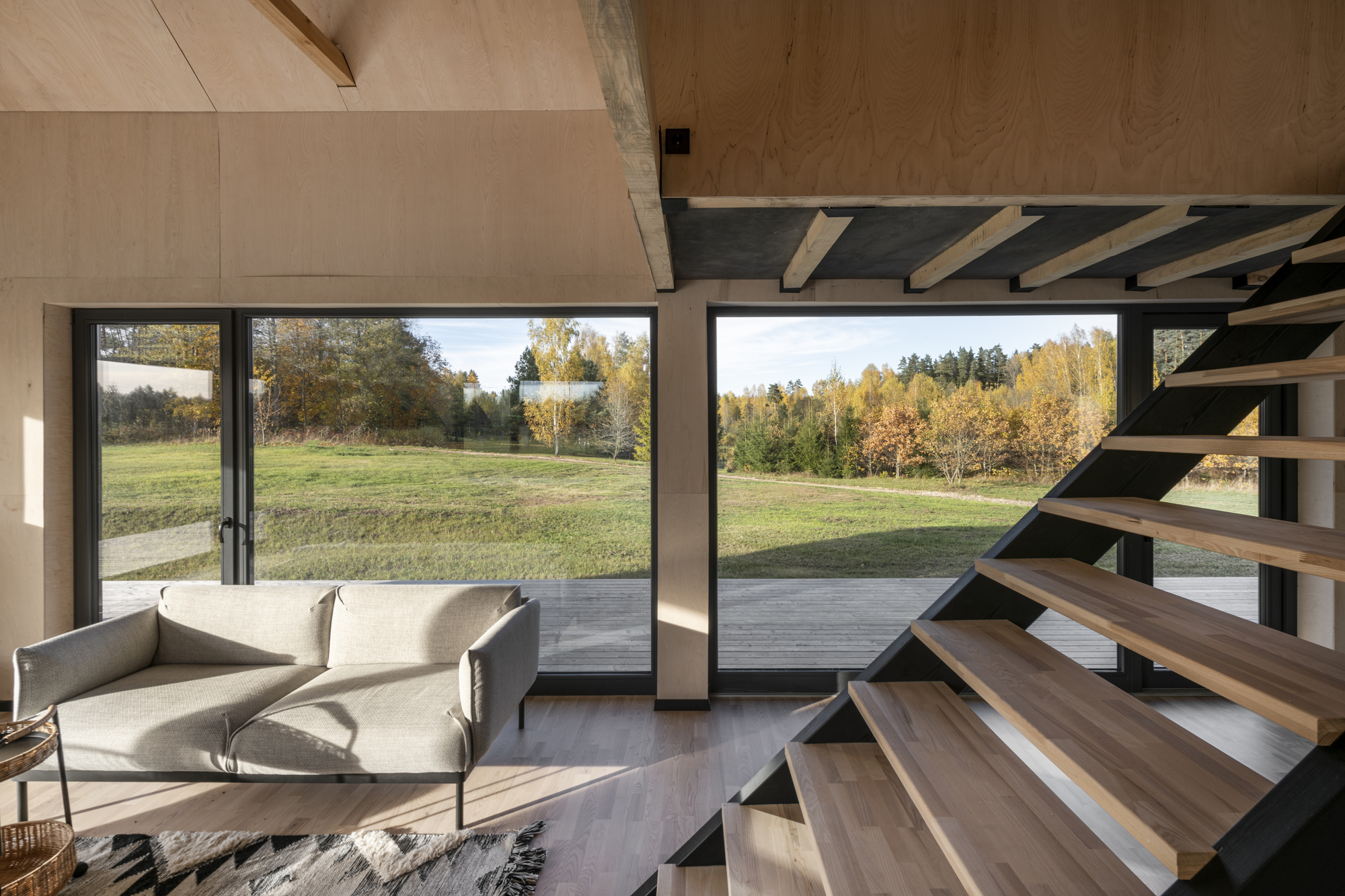 Living area with black steel staircase ascending past floor-to-ceiling glazed doors overlooking meadow