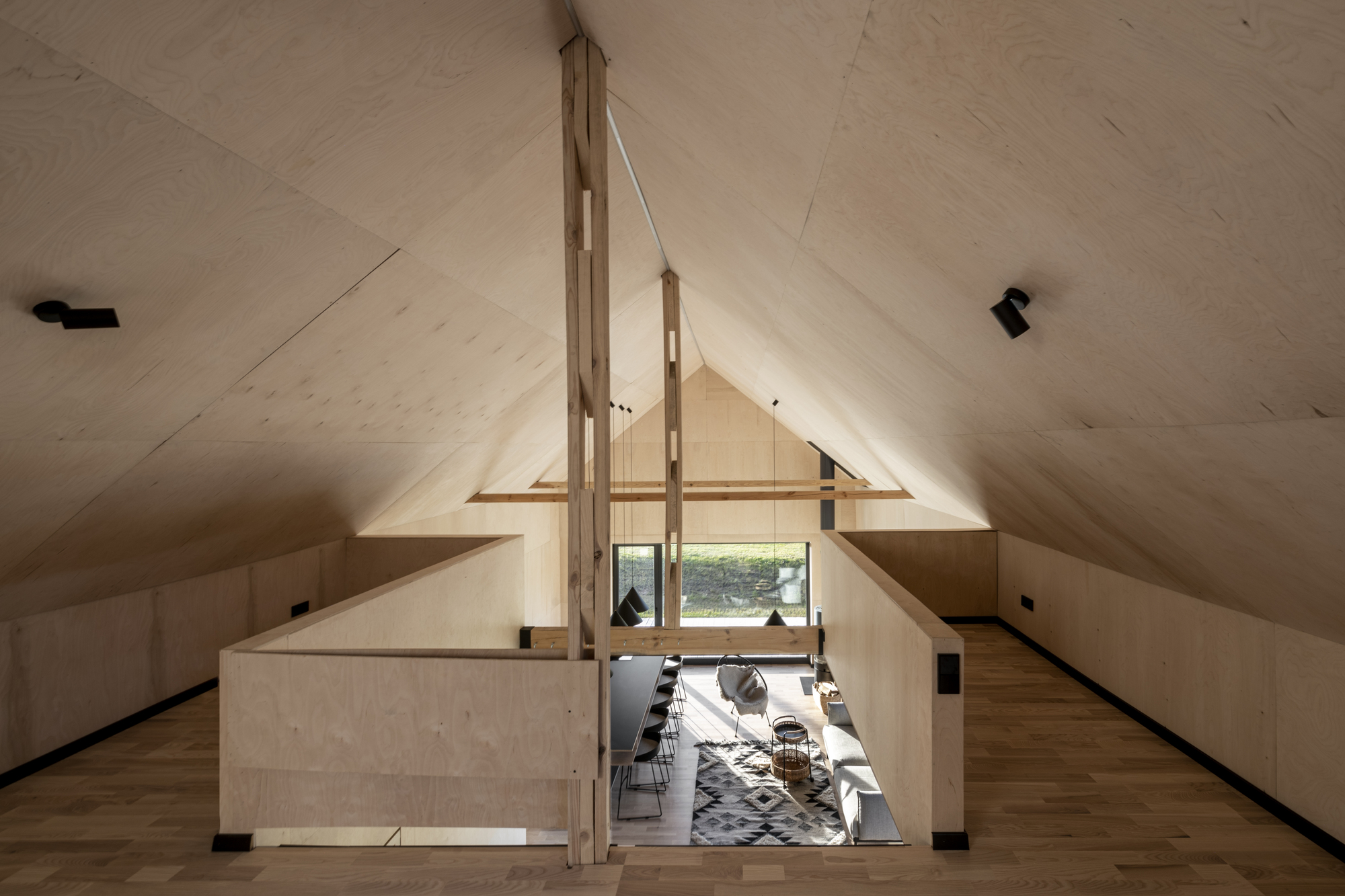 View from the loft level showing the double-height living space with plywood ceilings and timber support beams
