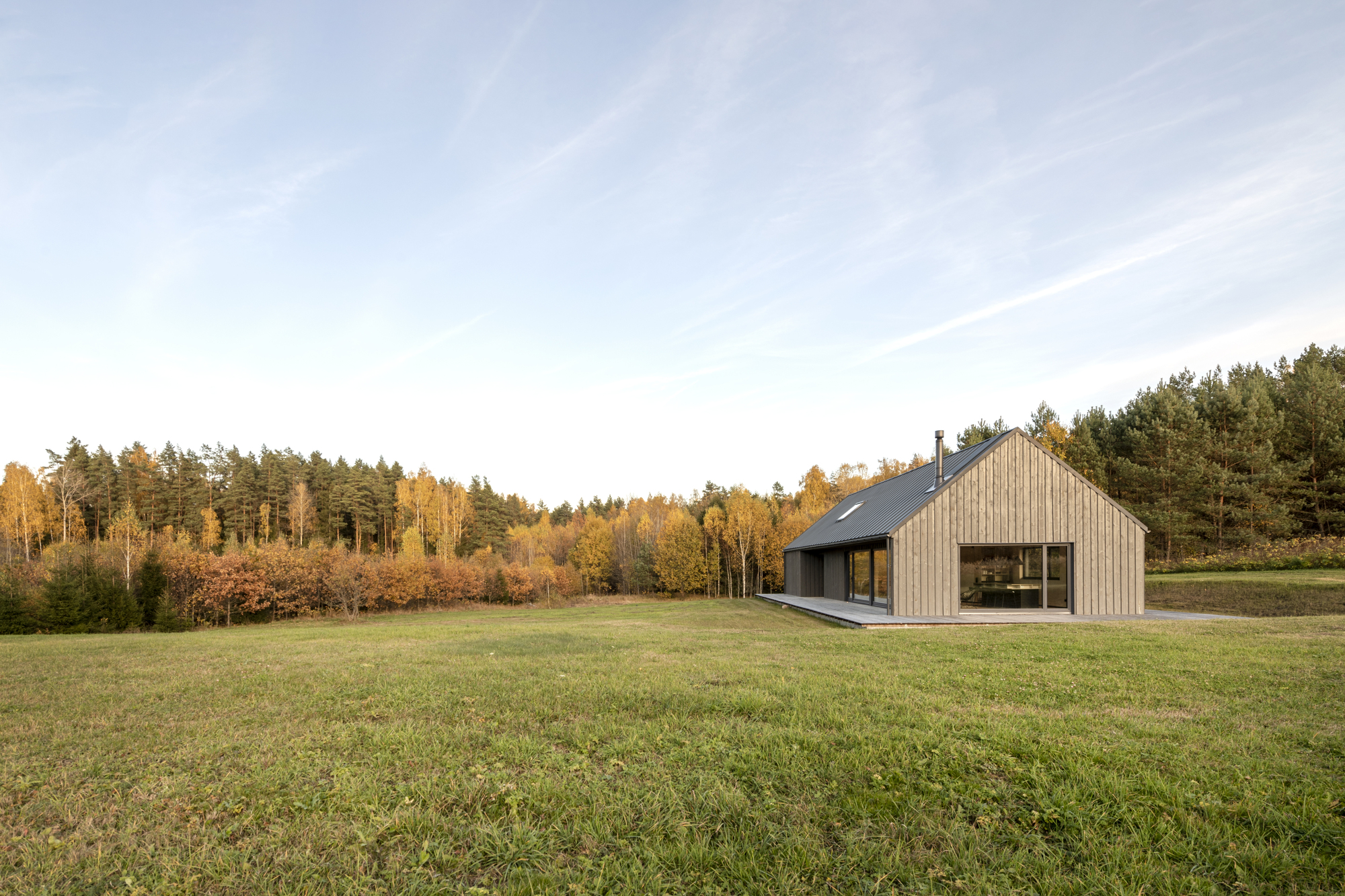 Distant view of the gabled volume in a grass field with forest treeline at golden hour