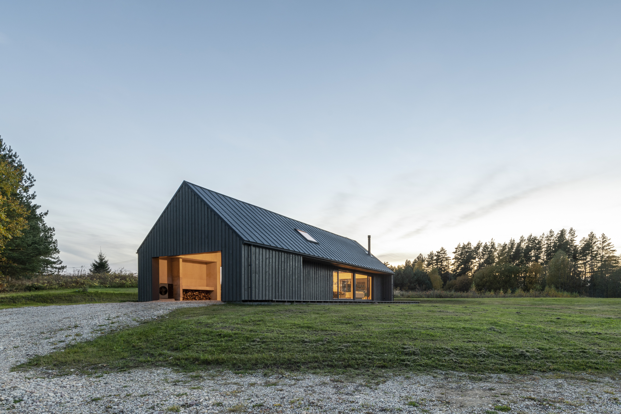 Gabled volume clad in vertical black metal siding with illuminated openings at dusk