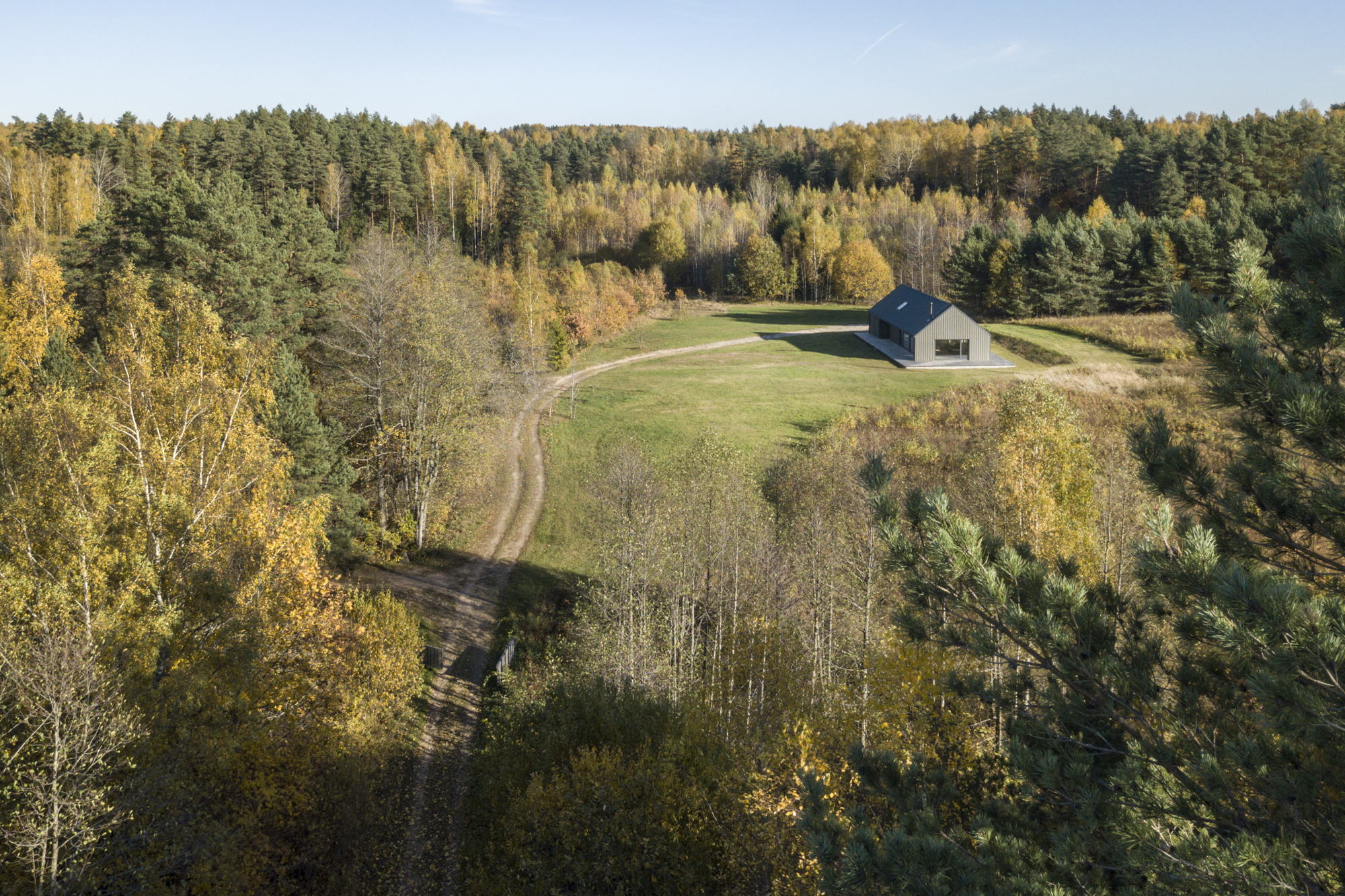 Drone view showing the dwelling positioned in a meadow clearing with winding dirt track