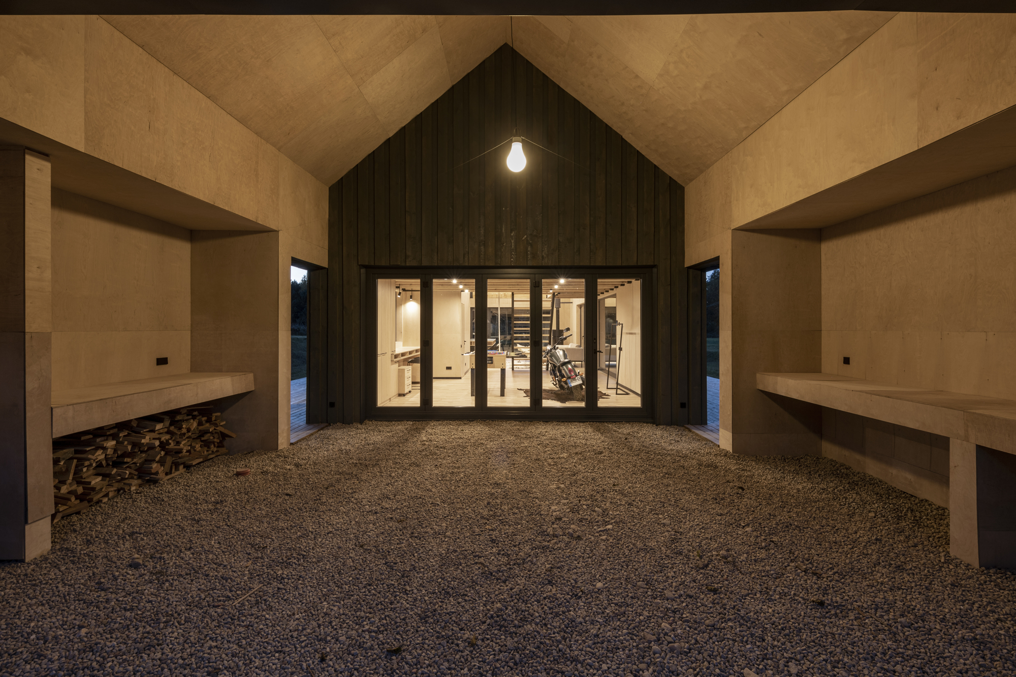 Covered entry courtyard with gravel floor and timber-clad volume lit from within at dusk