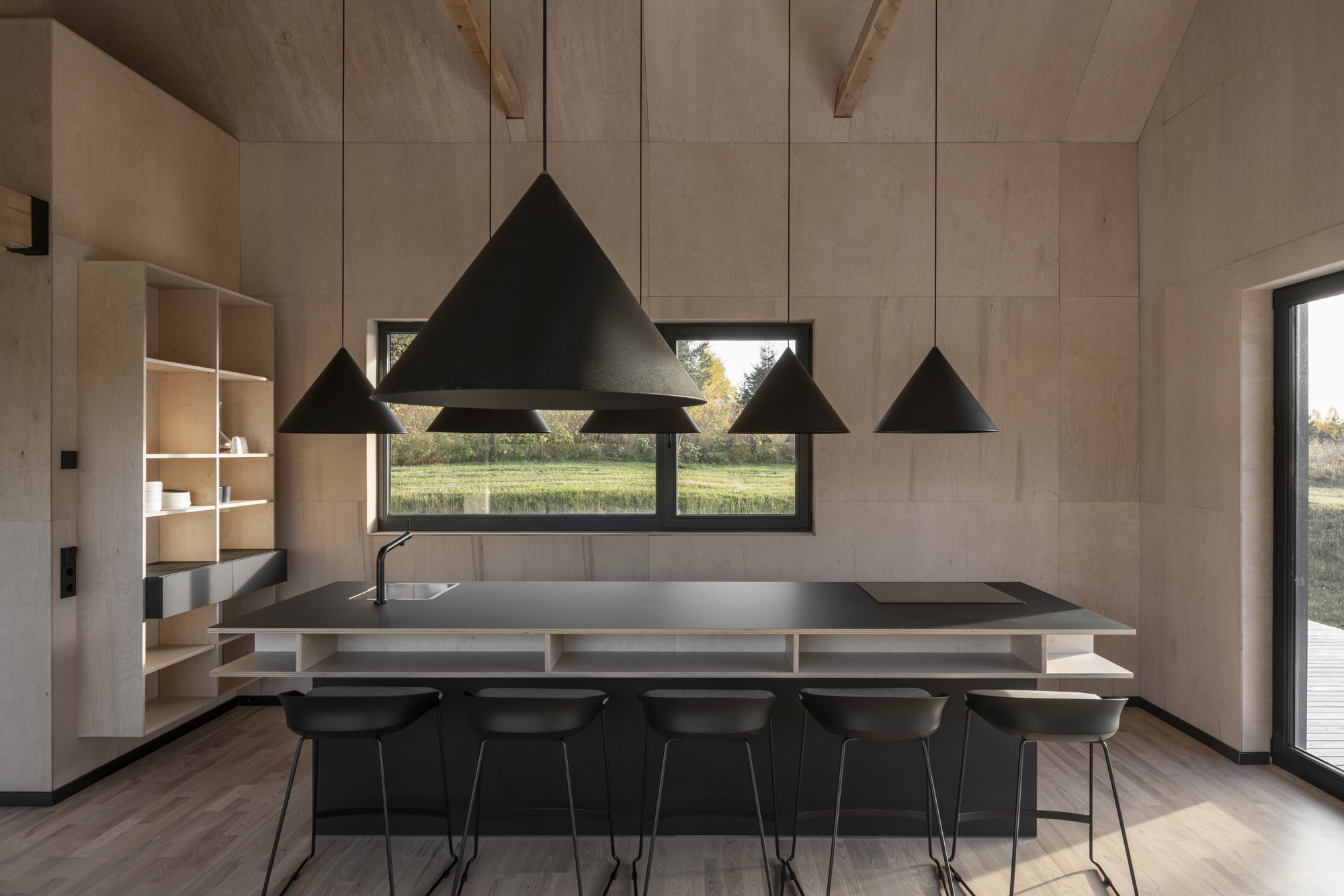 Kitchen island with black metal countertop beneath four triangular pendant lights and horizontal window framing landscape
