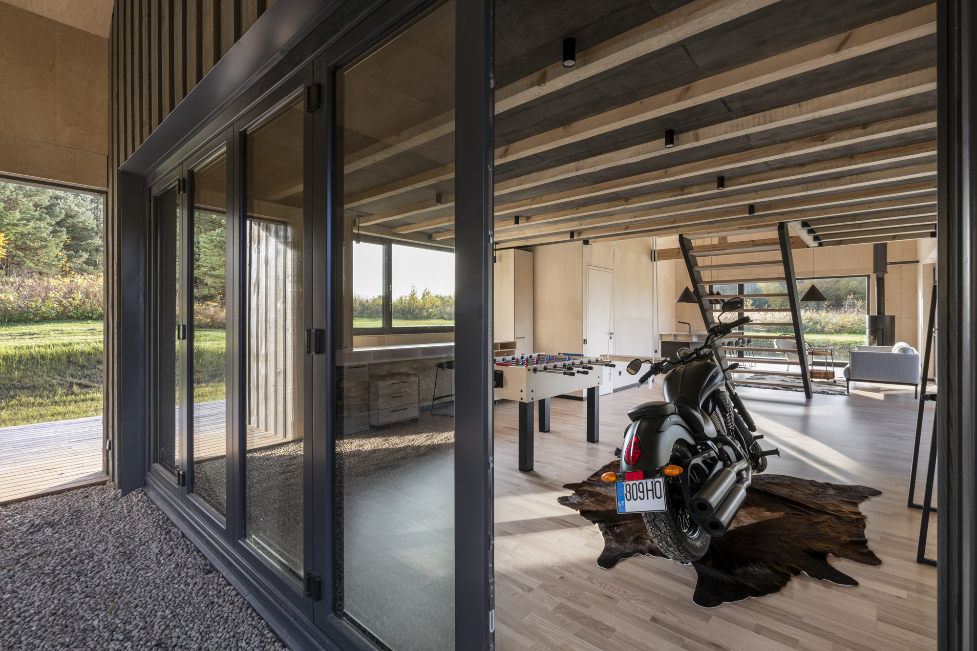 View through folding glass doors to interior with motorcycle and exposed timber rafters overhead