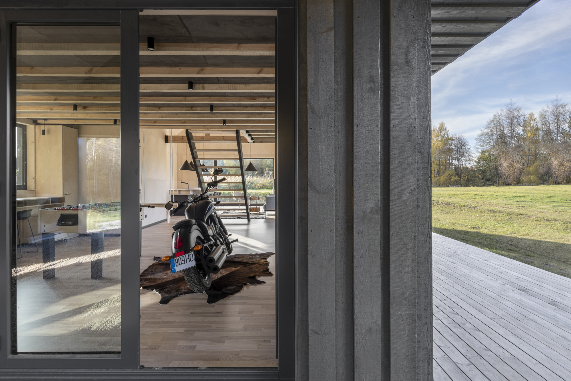 Close-up of charred timber cladding beside open glazed doors revealing interior with motorcycle and autumn landscape
