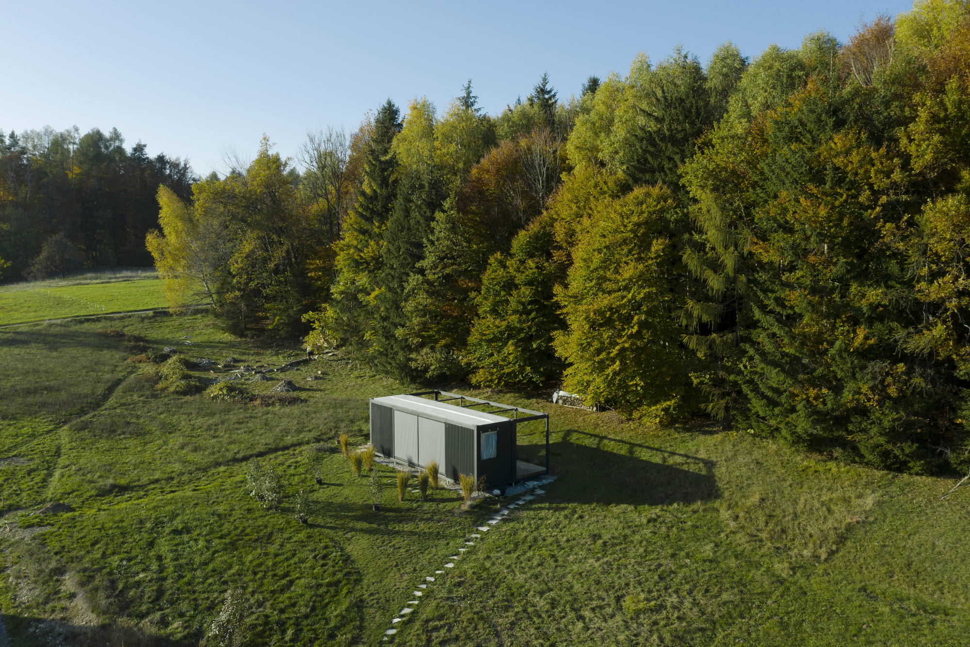 Aerial view of the rectangular pavilion sited in a sloping meadow beside a forest edge