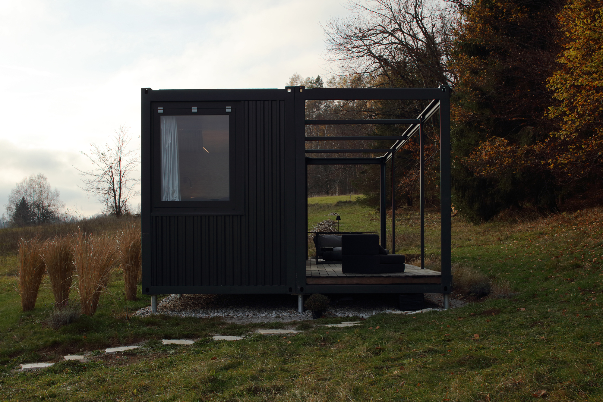Black corrugated metal volume with attached steel-framed terrace set in grassy landscape with bare trees