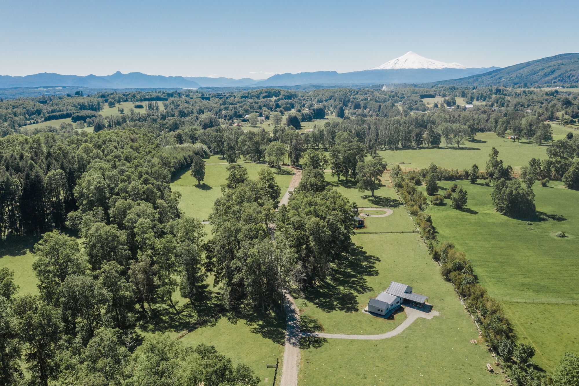Aerial view of the house and outbuilding amid fields and tree groves with a distant snowcapped peak