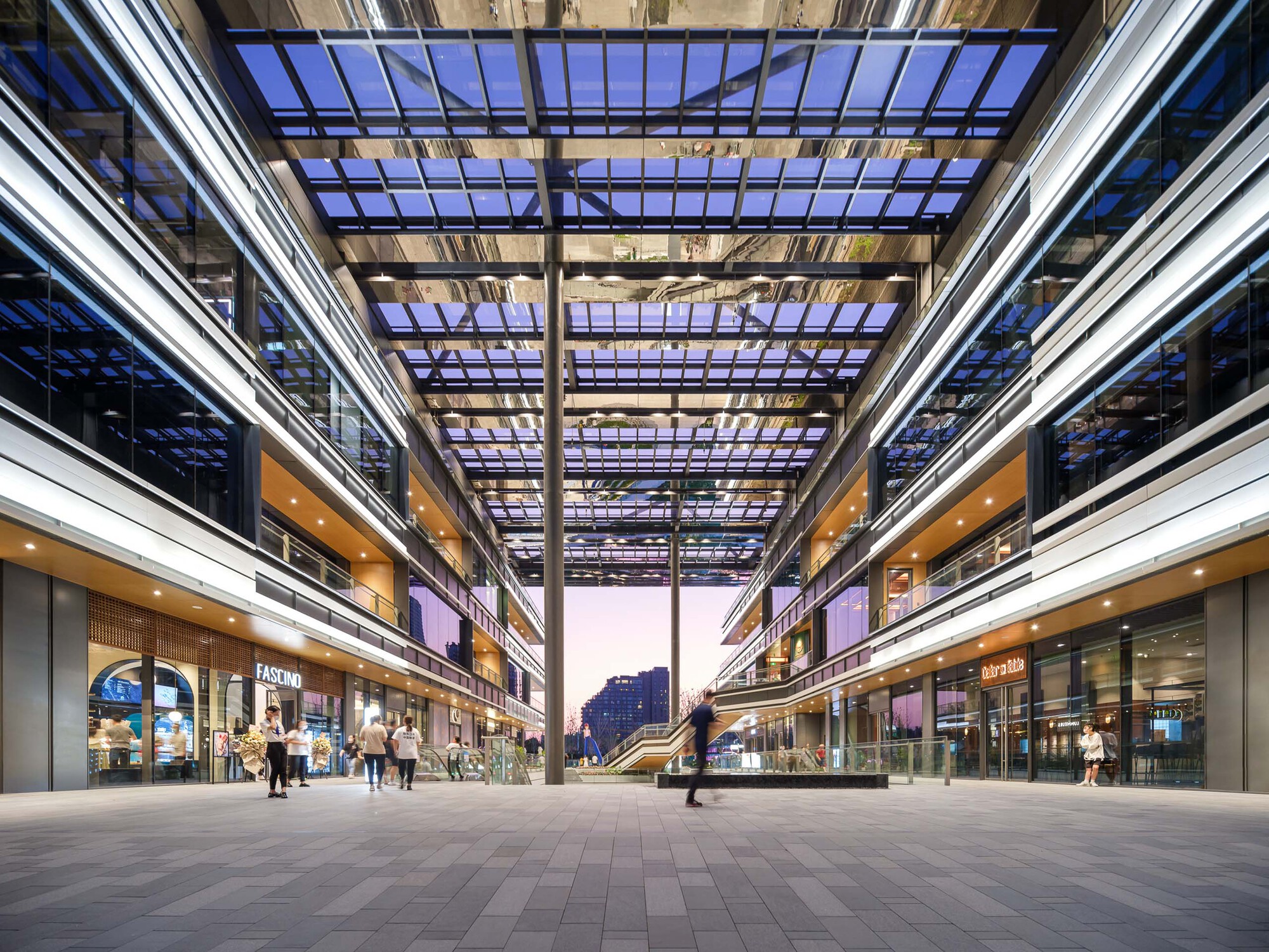 Open courtyard looking through the gridded steel and glass canopy at dusk with retail storefronts