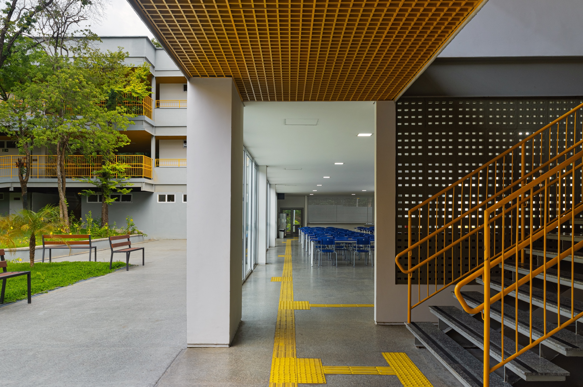 Covered walkway framing the courtyard with yellow tactile paving leading toward glazed interior spaces