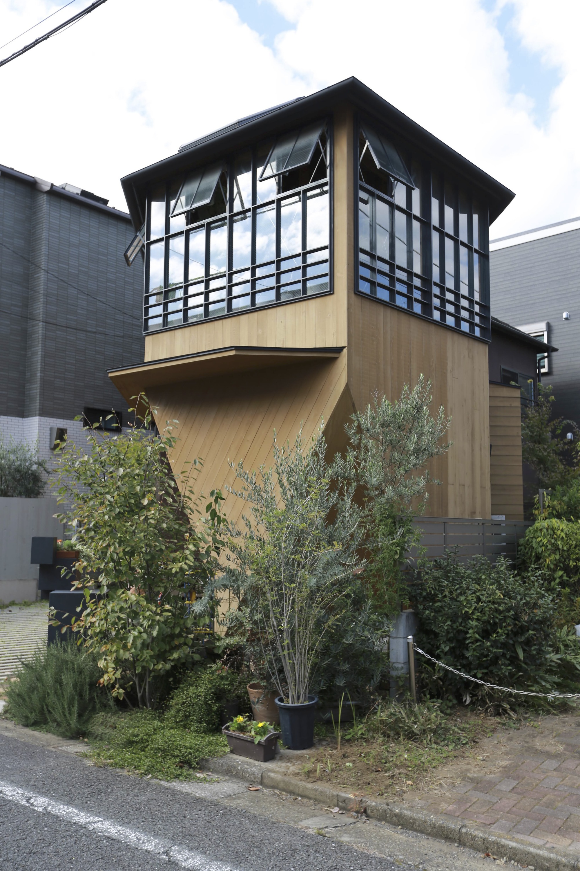 Garden approach showing the projecting upper floor clad in timber above potted plants