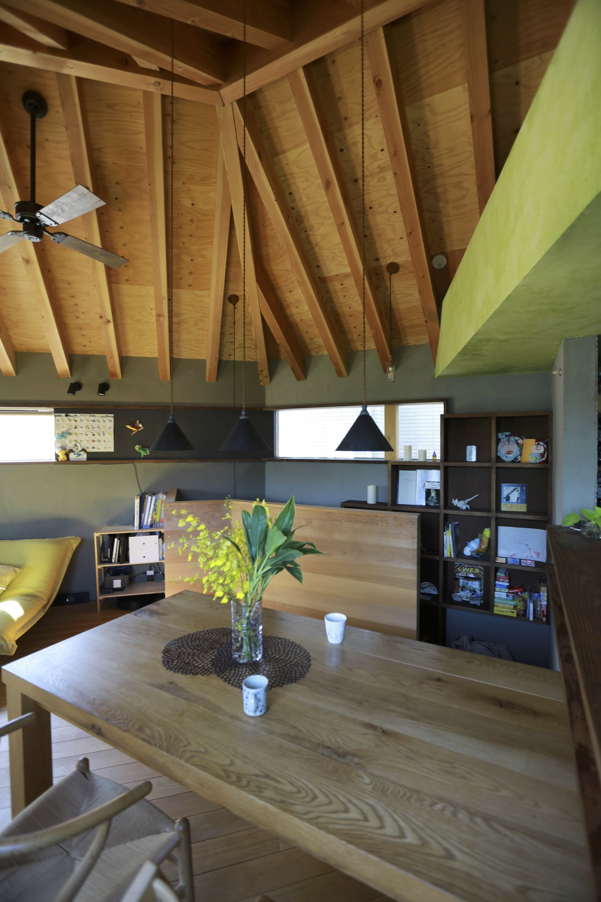 Dining area beneath curving exposed timber beams with black pendant lights and open shelving