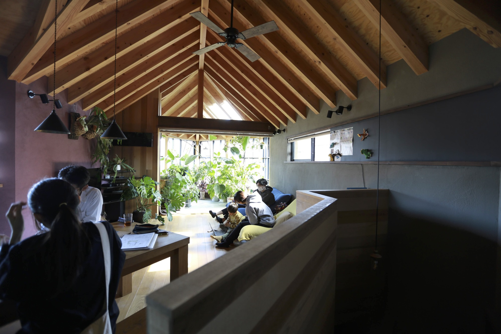 Long view across timber dining table toward inhabitants beneath the vaulted rafter ceiling
