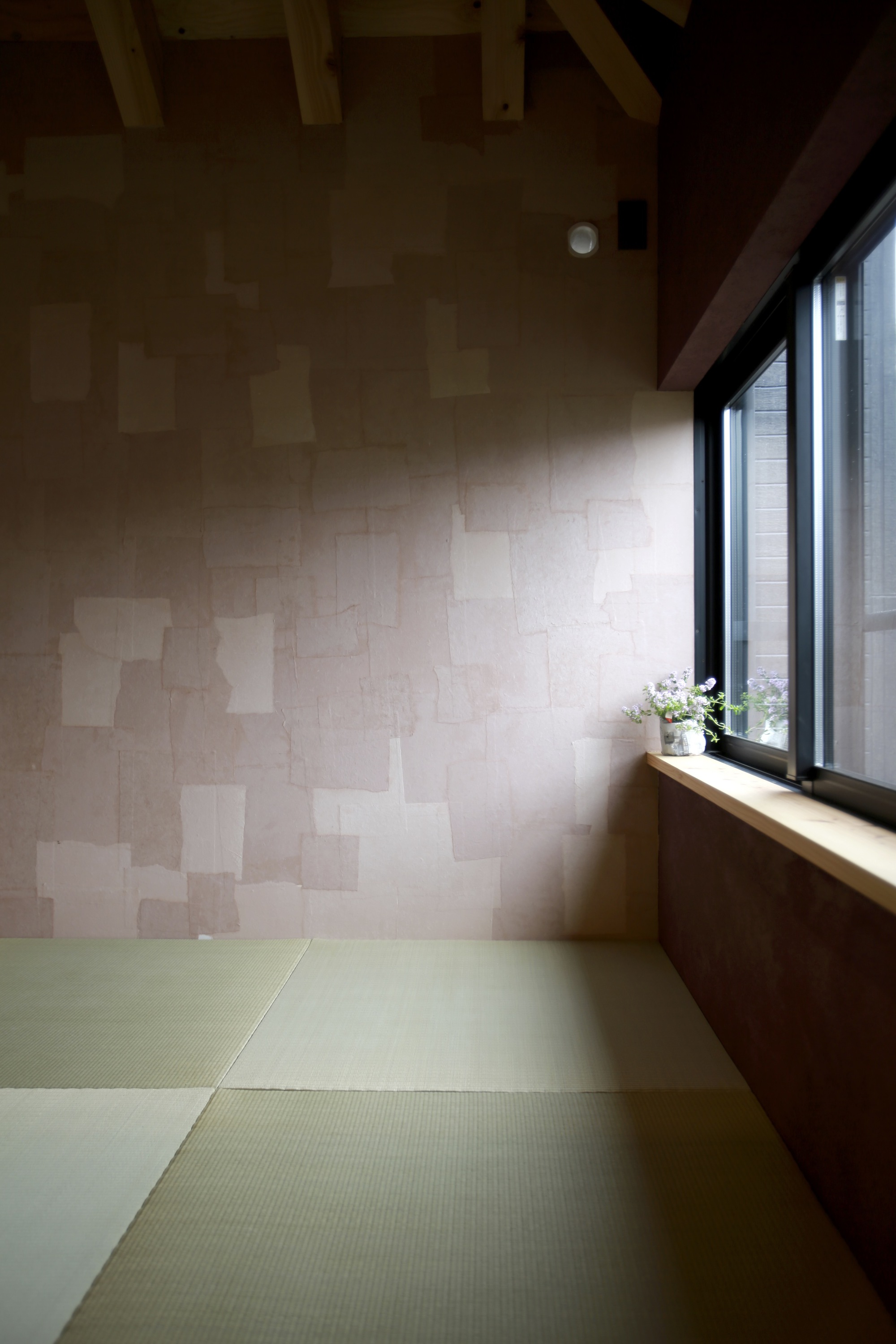 Tatami mat floor meeting a patchwork plywood wall beneath a timber beam ceiling