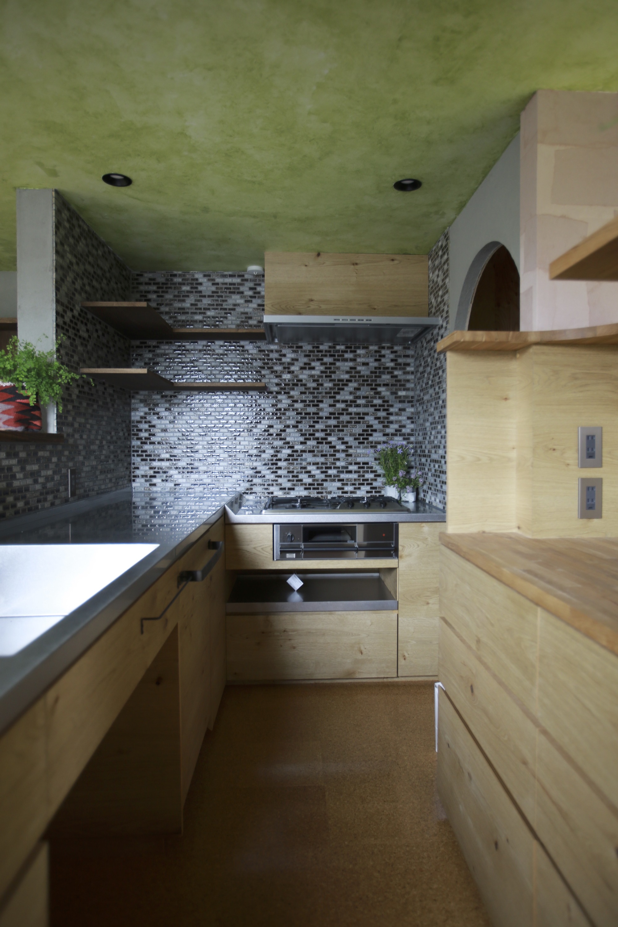 Compact kitchen with black mosaic tile backsplash and lime green ceiling above timber counters