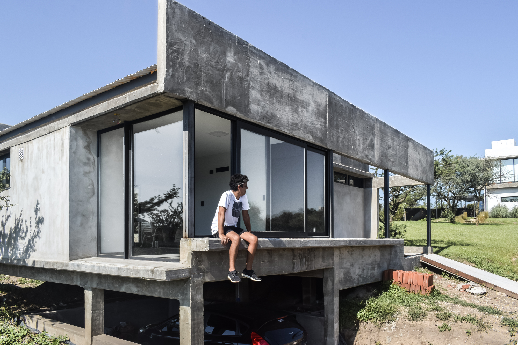 Corner terrace with concrete deck and a person seated at the edge overlooking the carport below