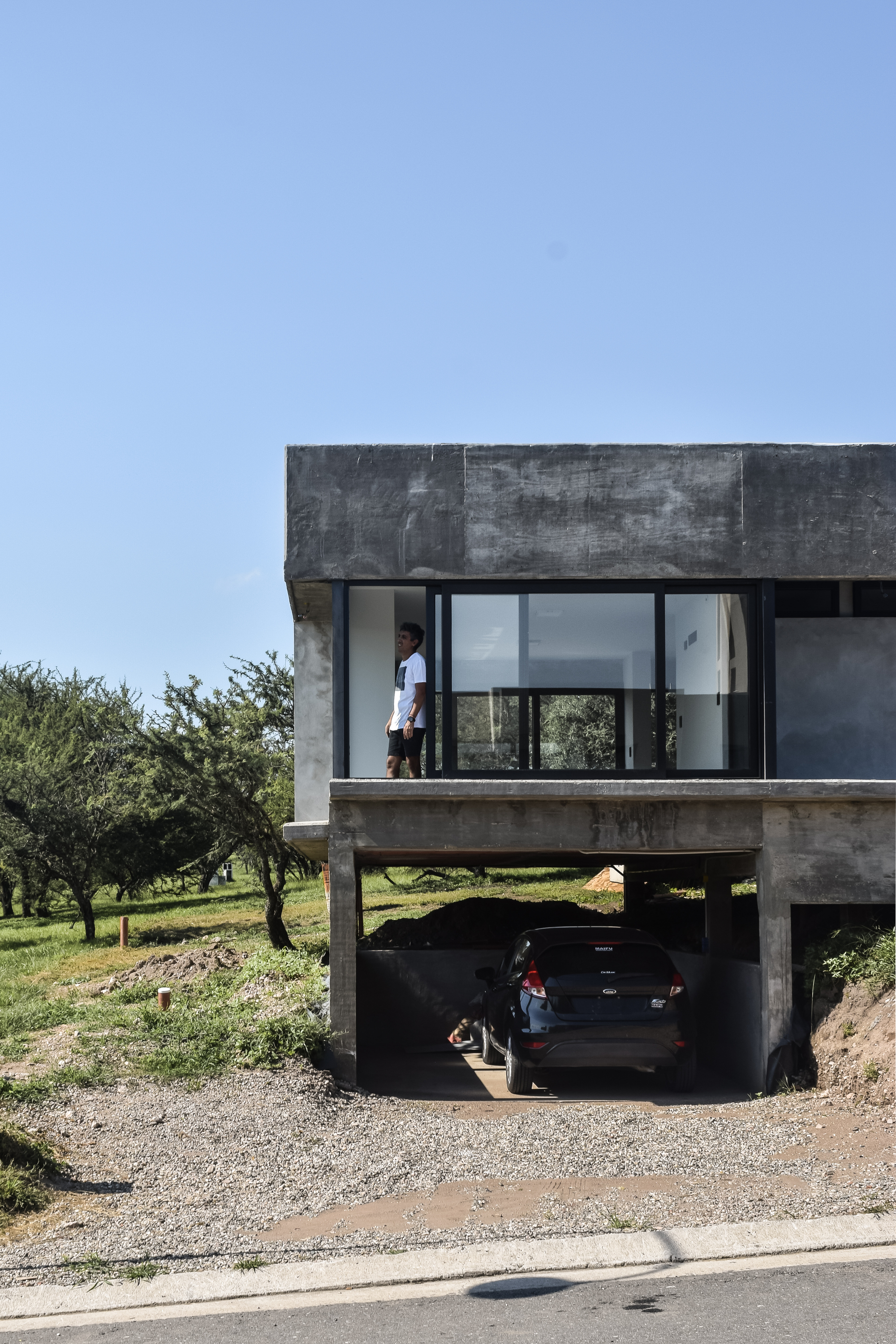 Concrete piloti structure supporting the glazed upper level above an open carport with parked car